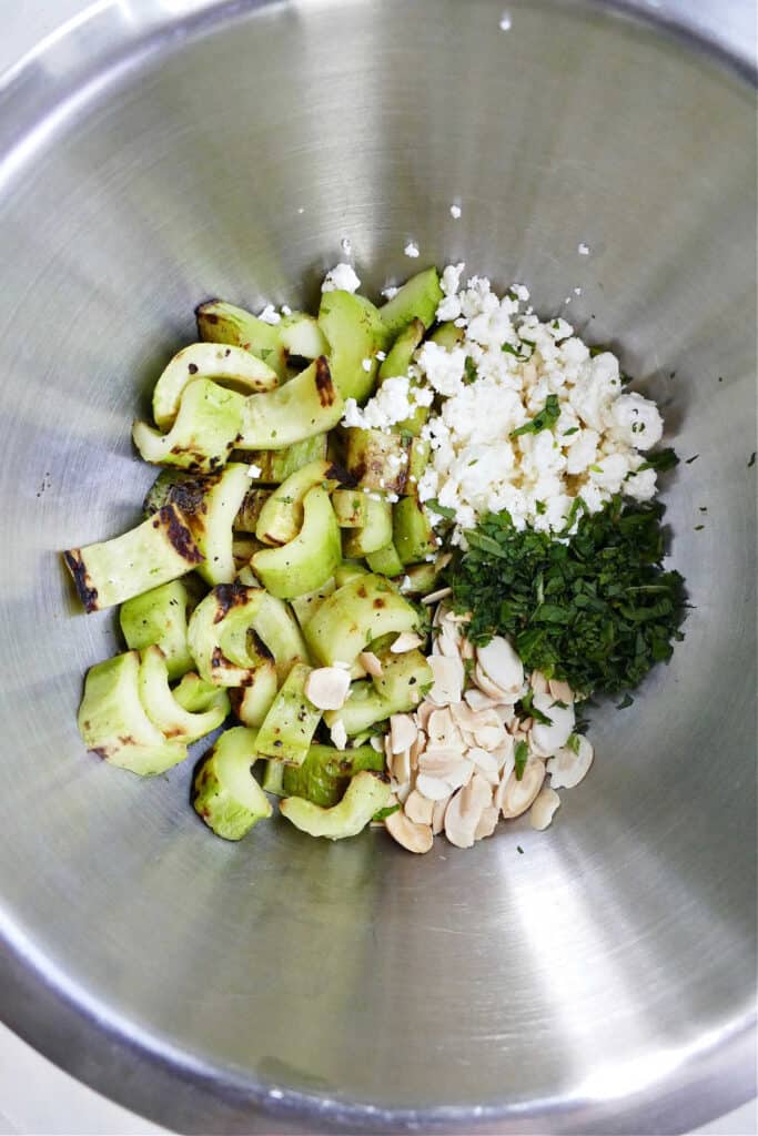 grilled cucumber, feta cheese, mint, and toasted almonds in a mixing bowl