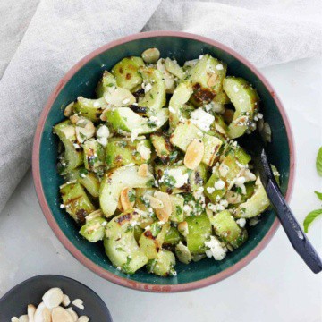 grilled cucumber with feta and mint in a serving bowl with a spoon on a counter