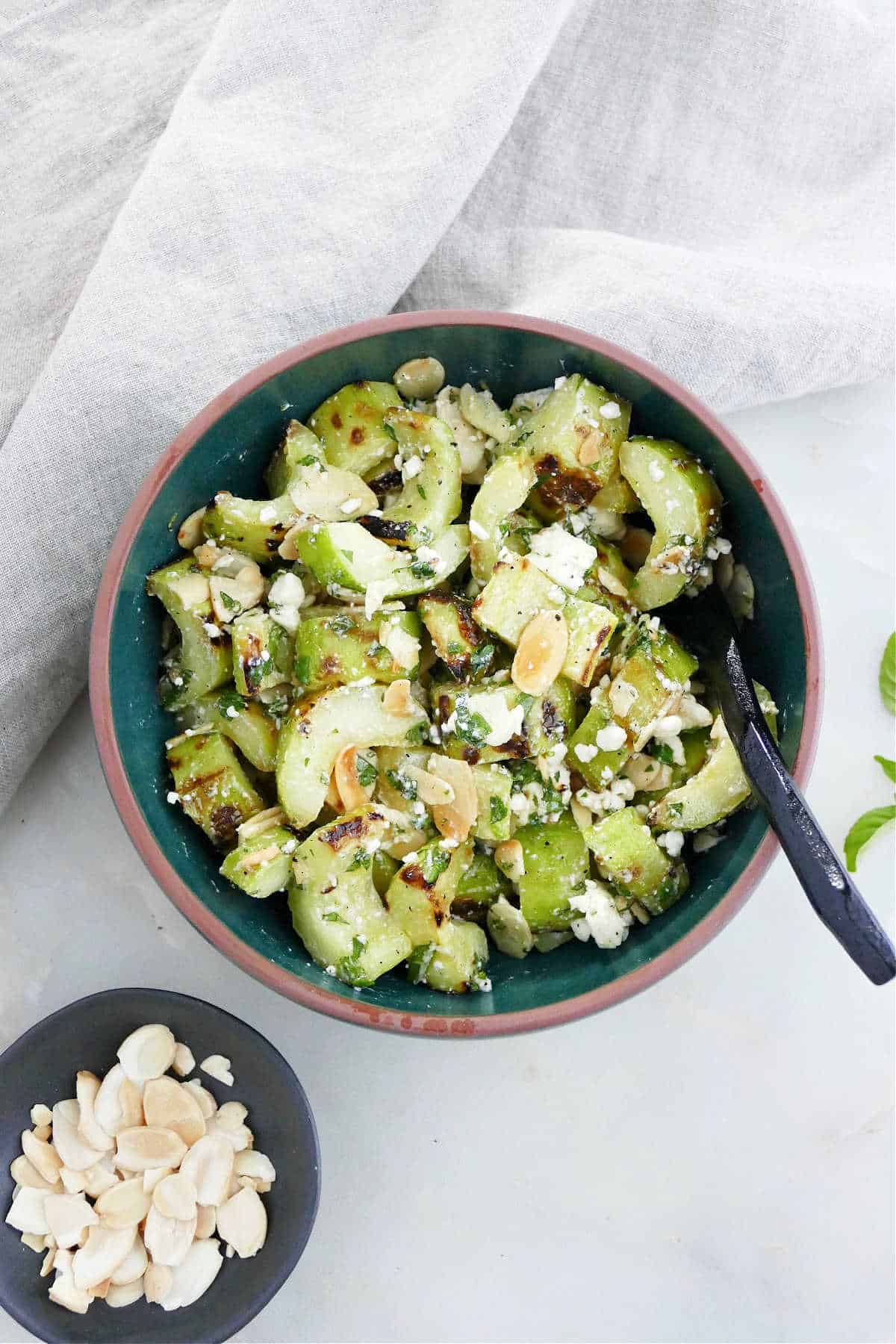 grilled cucumber with feta and mint in a serving bowl with a spoon on a counter