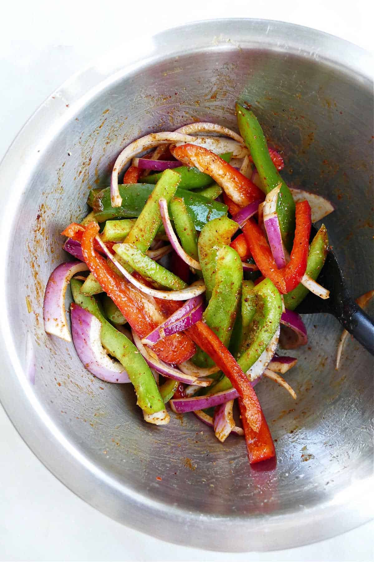 sliced peppers and onions mixed with oil and seasonings in a bowl on a counter