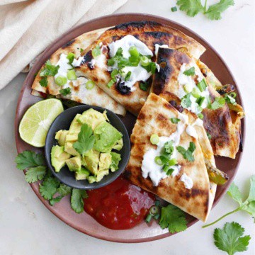 grilled quesadilla sliced into four pieces on a plate with salsa, avocado, and lime