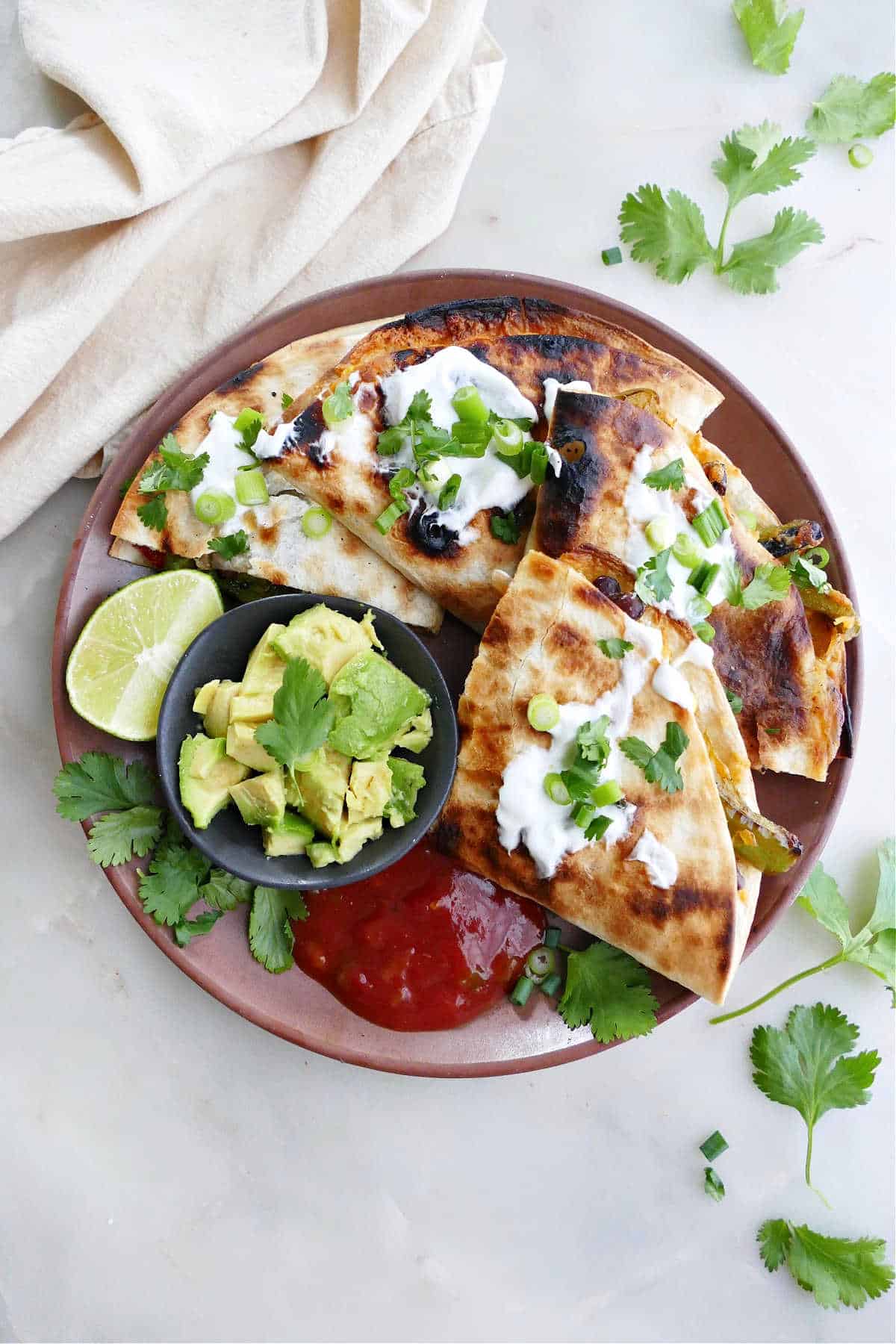grilled quesadilla sliced into four pieces on a plate with salsa, avocado, and lime