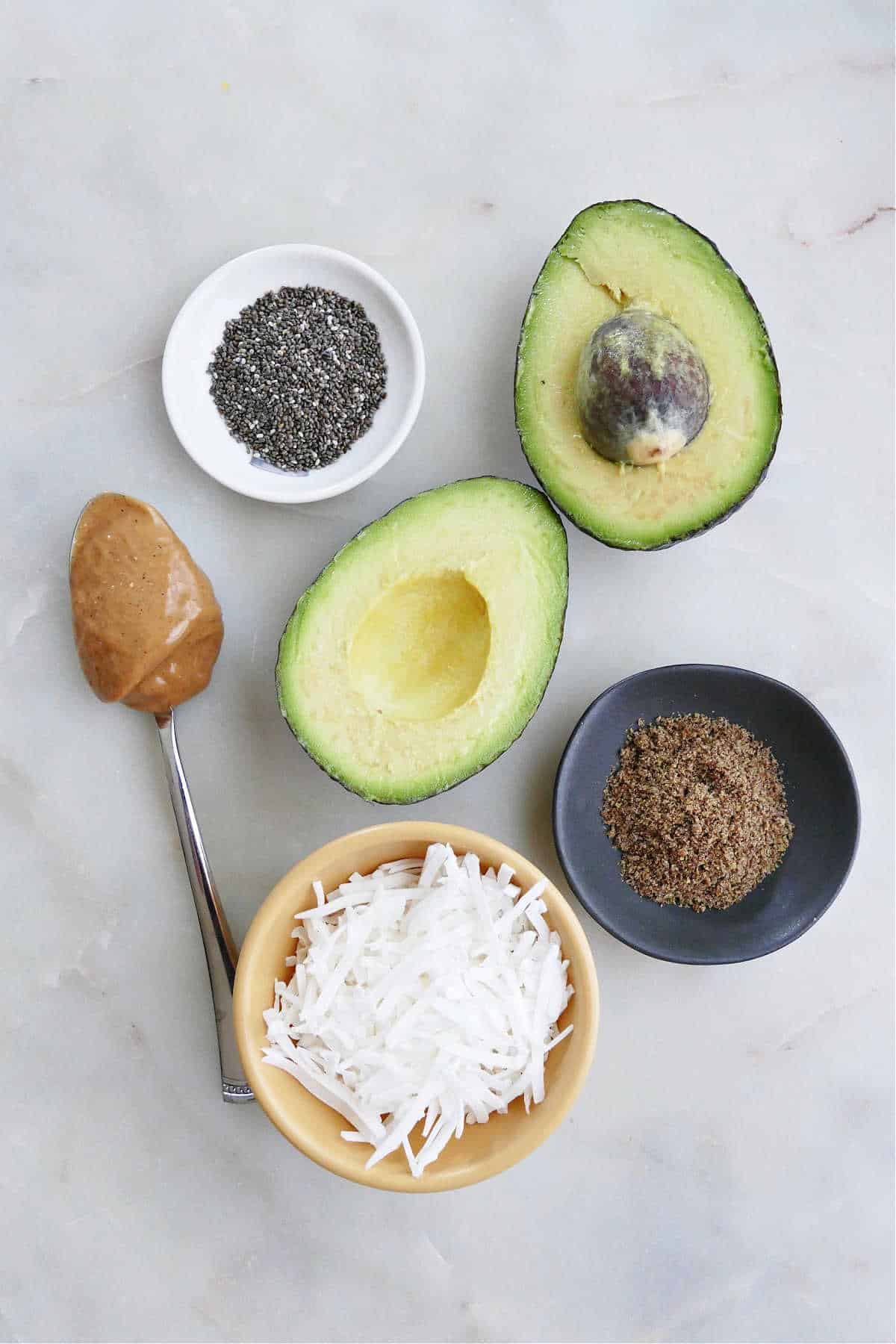 chia seeds, peanut butter, avocado, coconut, and flaxseed spread out on a counter