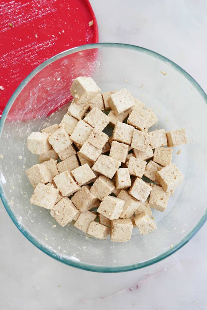tofu cubes with olive oil, soy sauce, and cornstarch in a glass bowl on a counter