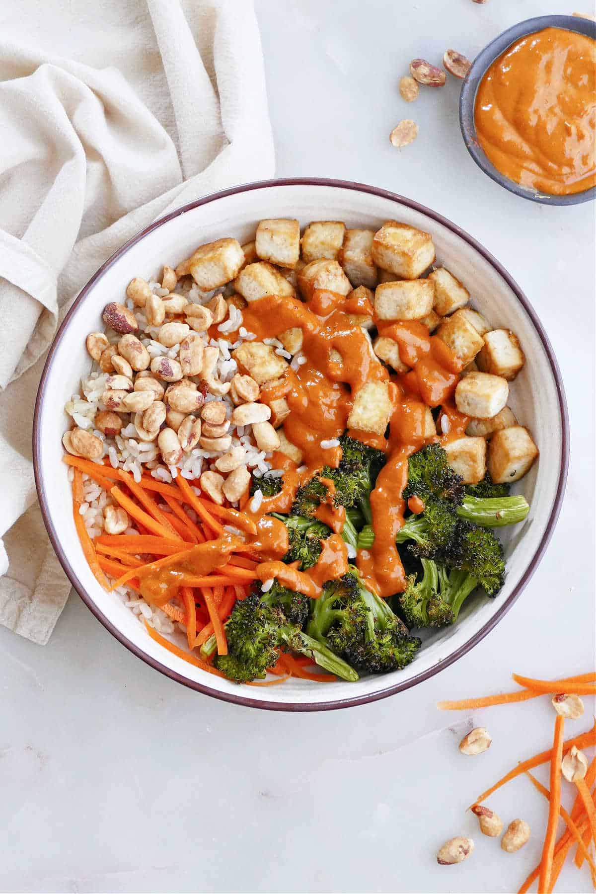 spicy peanut tofu buddha bowl on a counter surrounded by ingredients