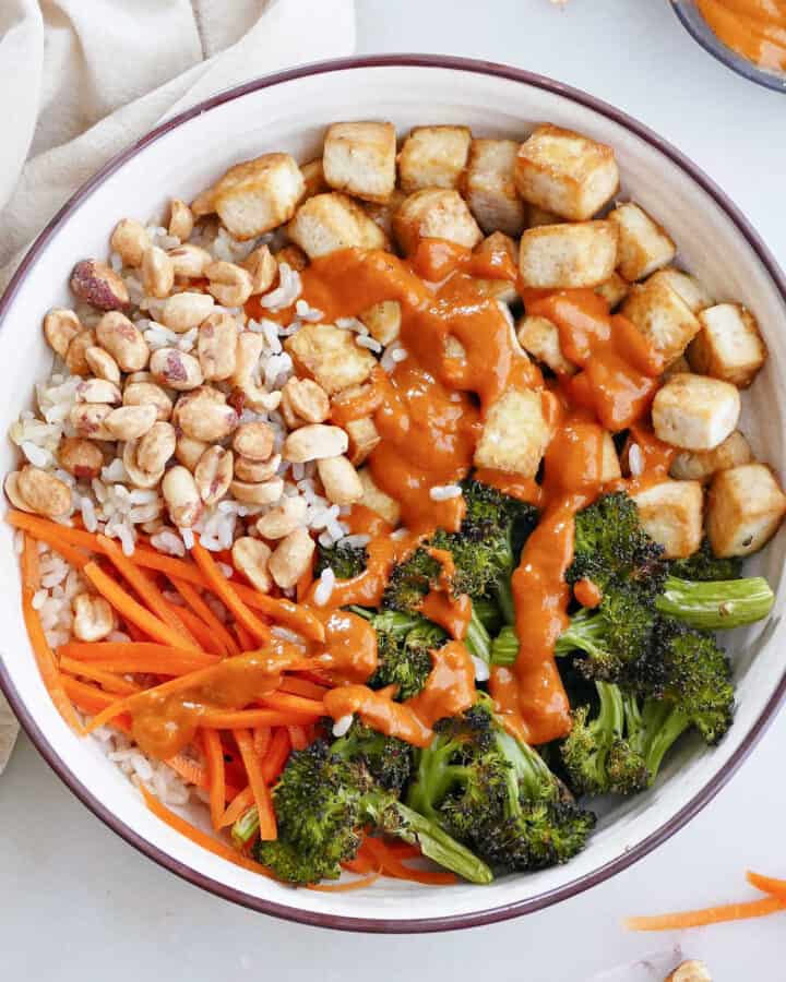 spicy peanut tofu buddha bowl on a counter surrounded by ingredients
