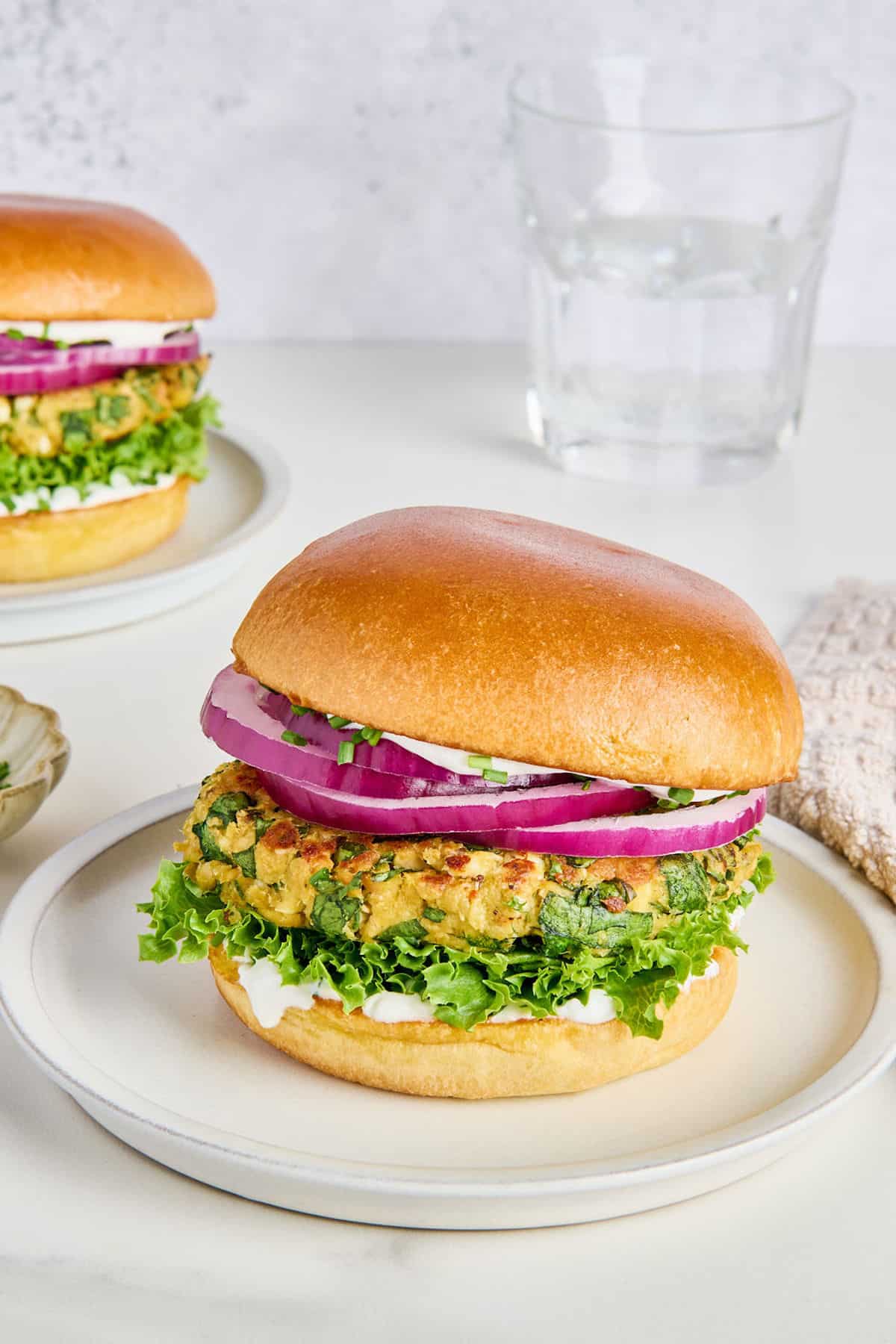 Salmon burger recipe on a bun with lettuce and onion on a plate.