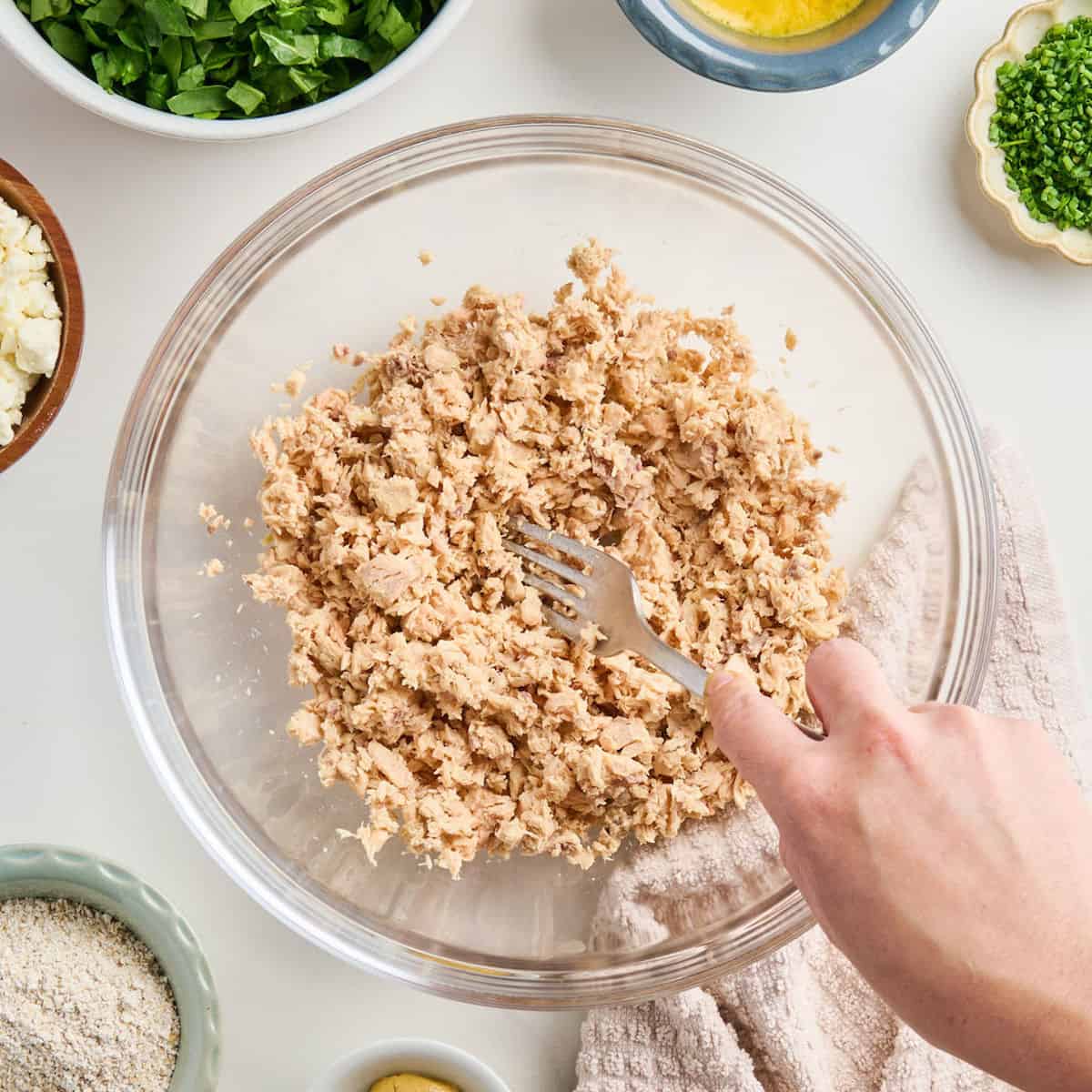 Woman flaking canned salmon with a fork in a glass mixing bowl.