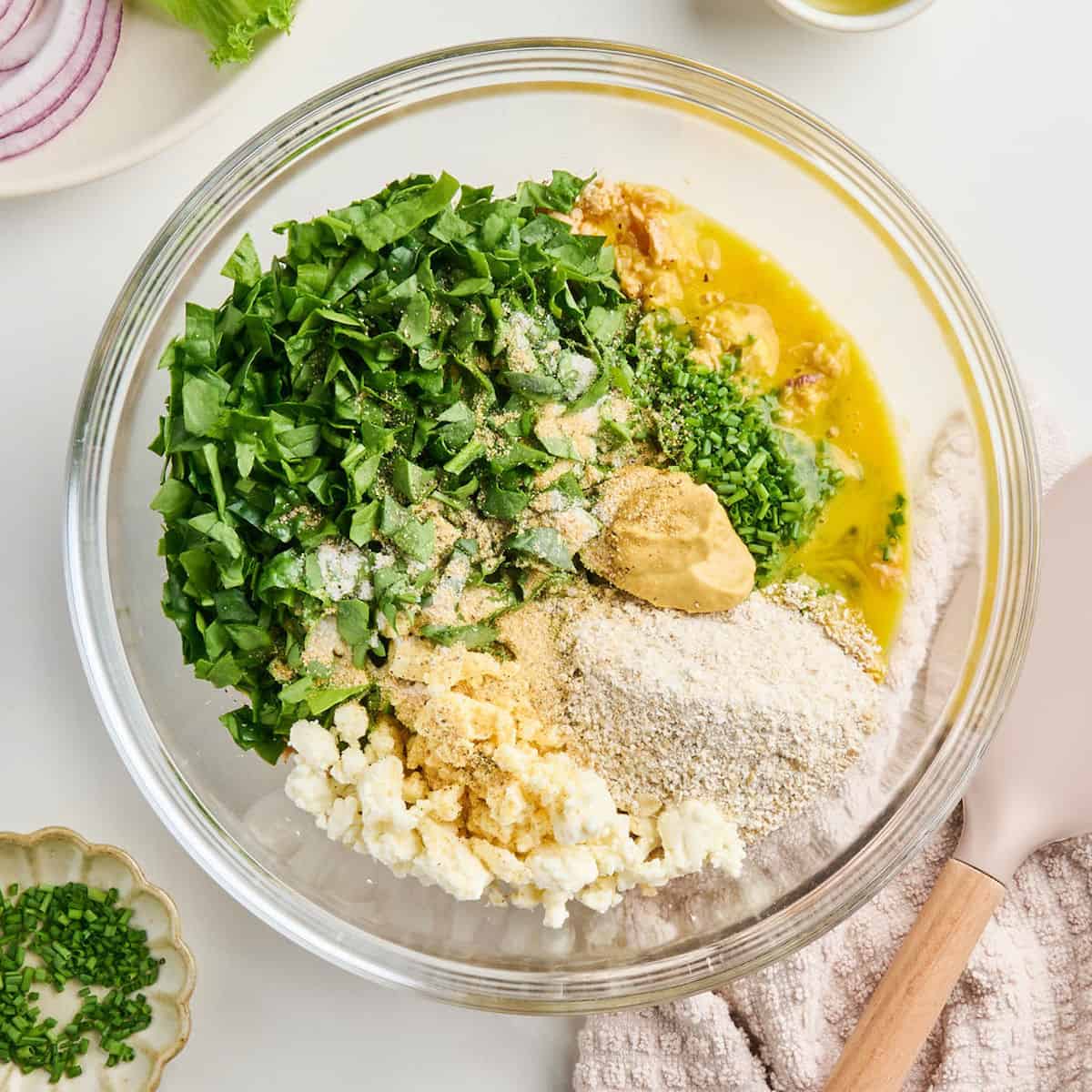 Spinach, ground oats, seasonings, feta, and beaten egg added to canned salmon in a bowl.