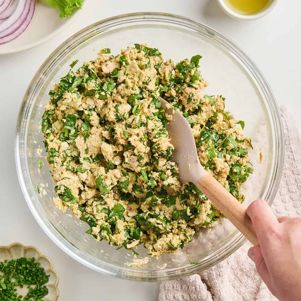 Woman mixing ingredients for a salmon burger recipe in a glass mixing bowl.