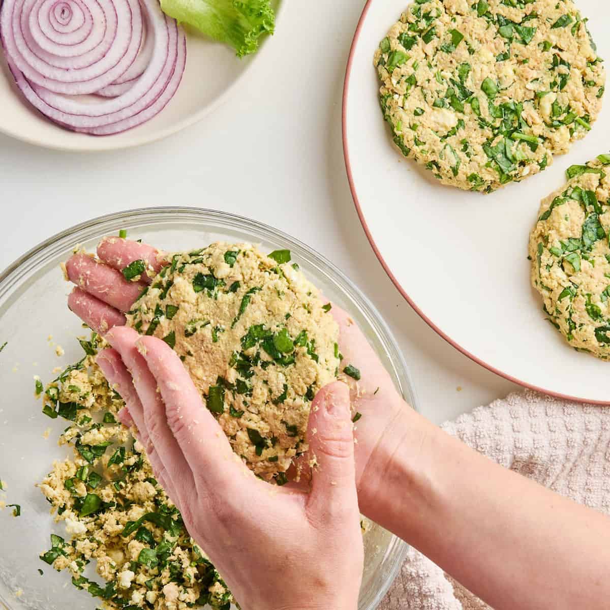 Woman forming a spinach feta salmon burger with her hands over a bowl.