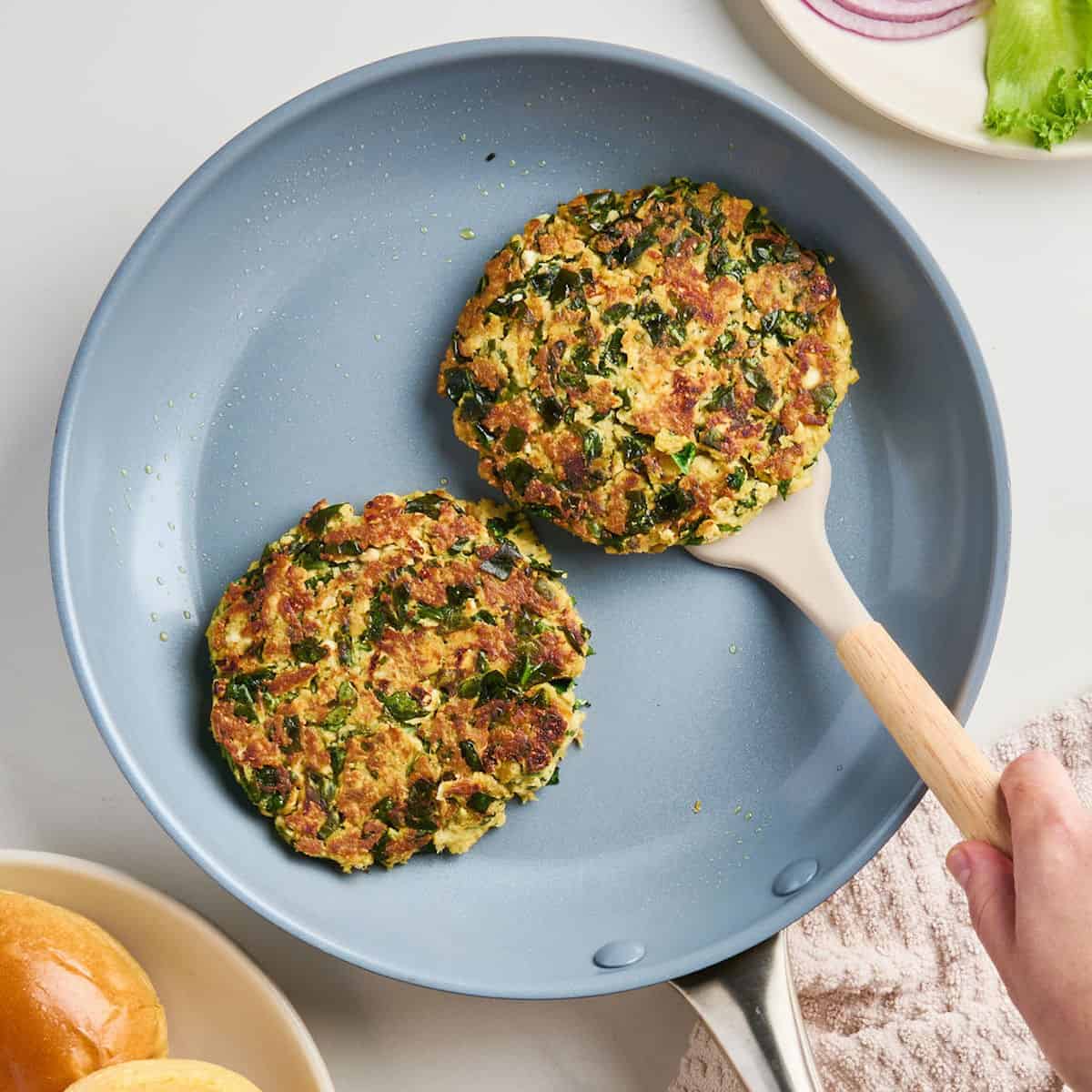 Woman turning a spinach feta salmon burger with a spatula in a nonstick skillet.