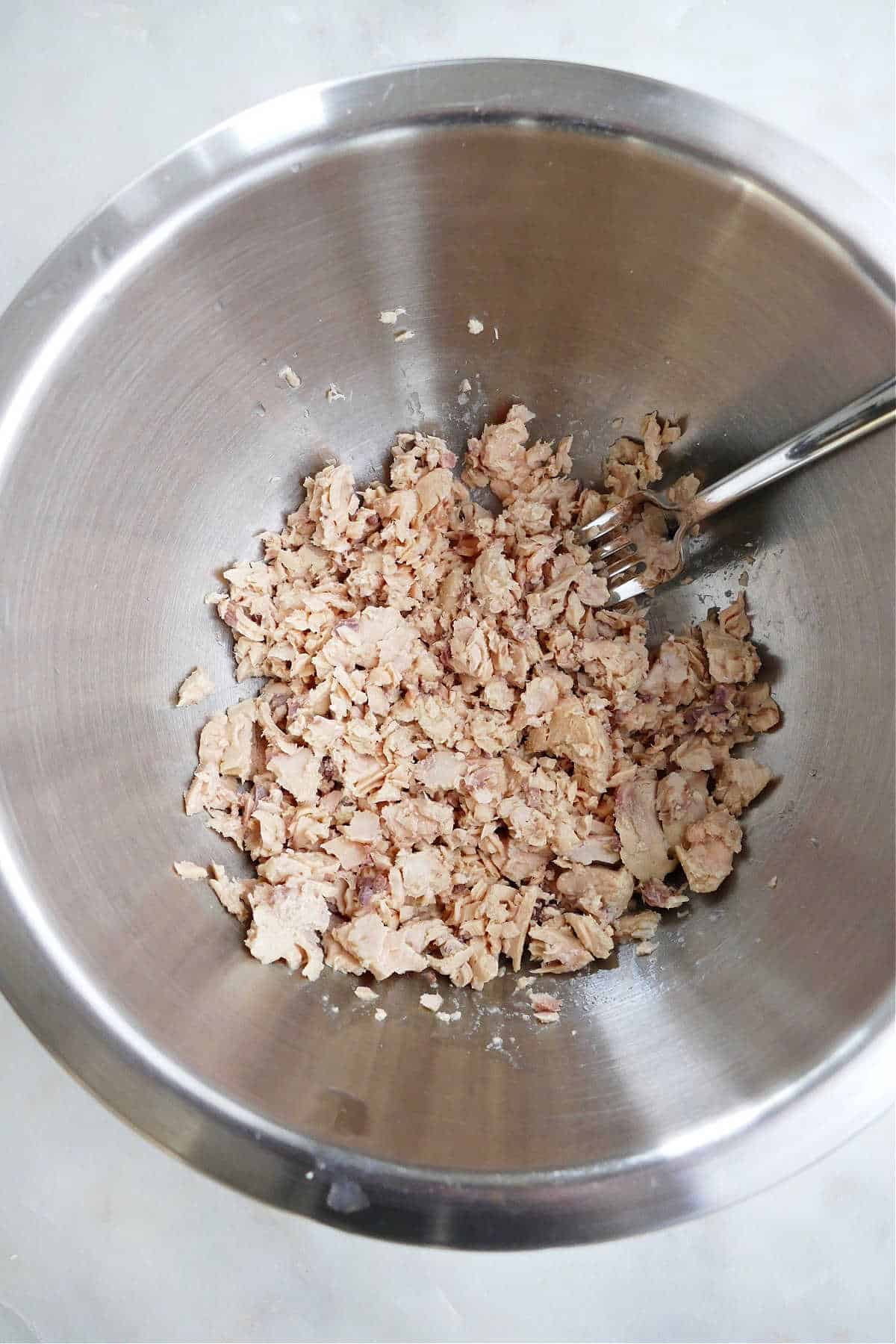 canned salmon being flaked with a fork in a mixing bowl