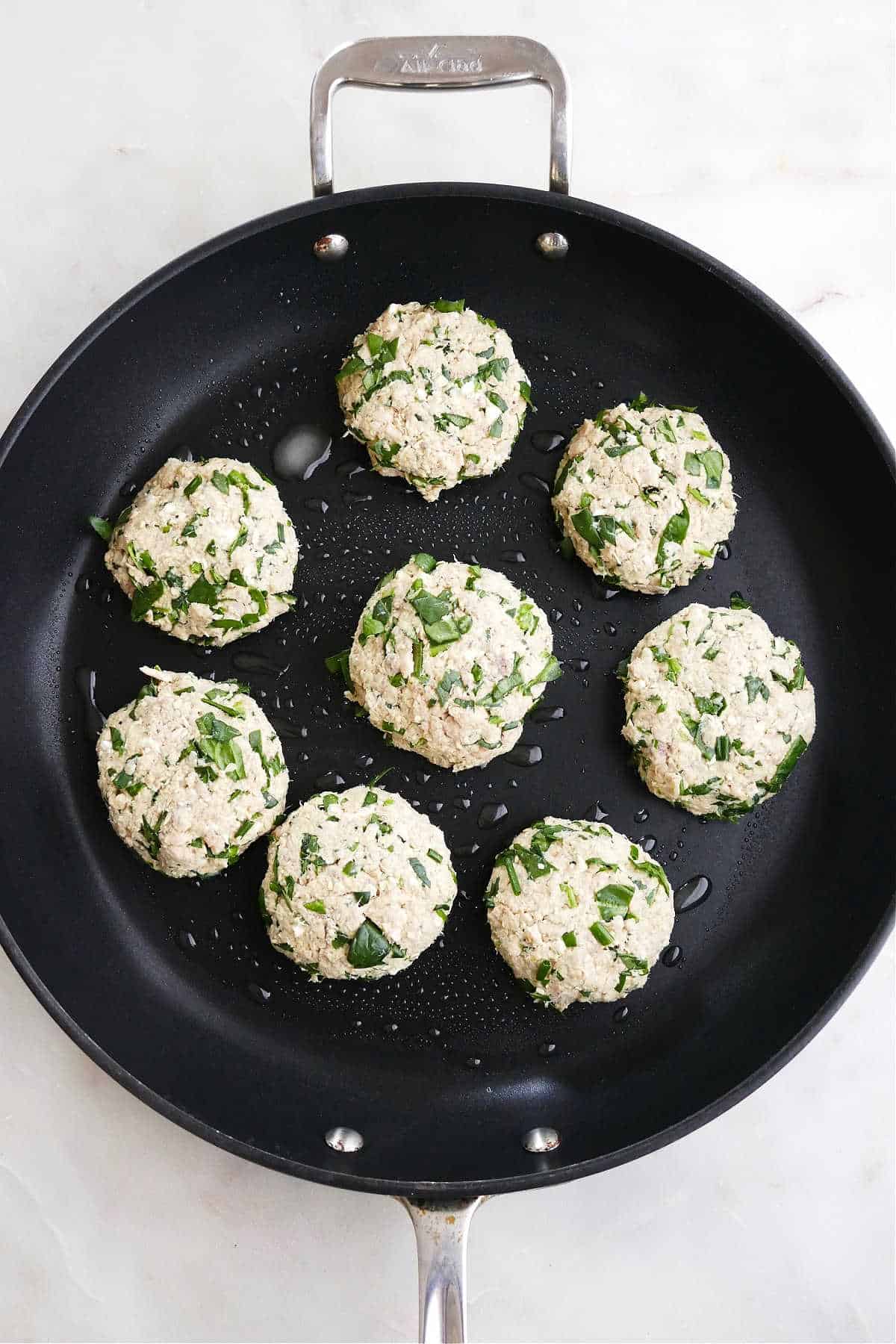 eight salmon burgers cooking in a large black skillet on a counter