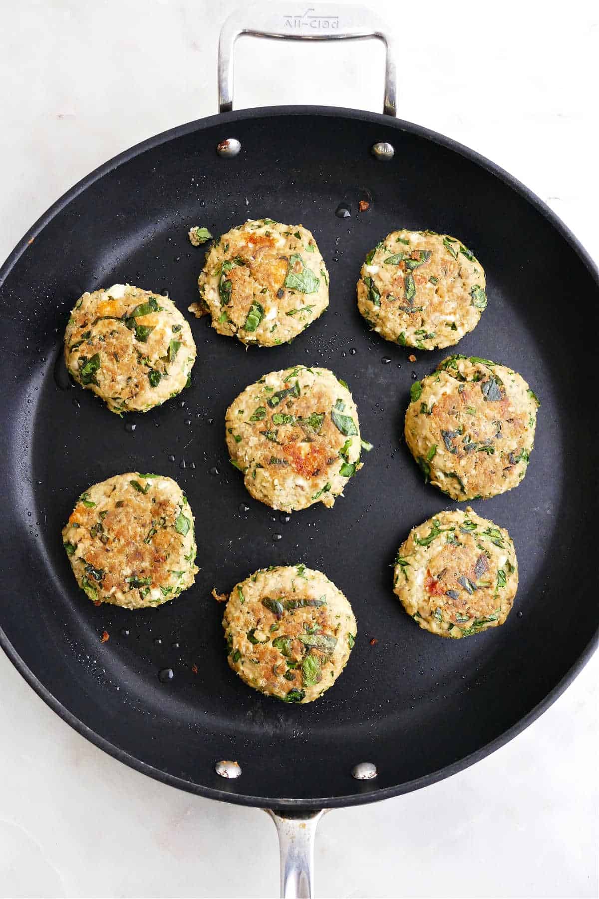 eight cooked spinach feta salmon burgers in a large black skillet on a counter