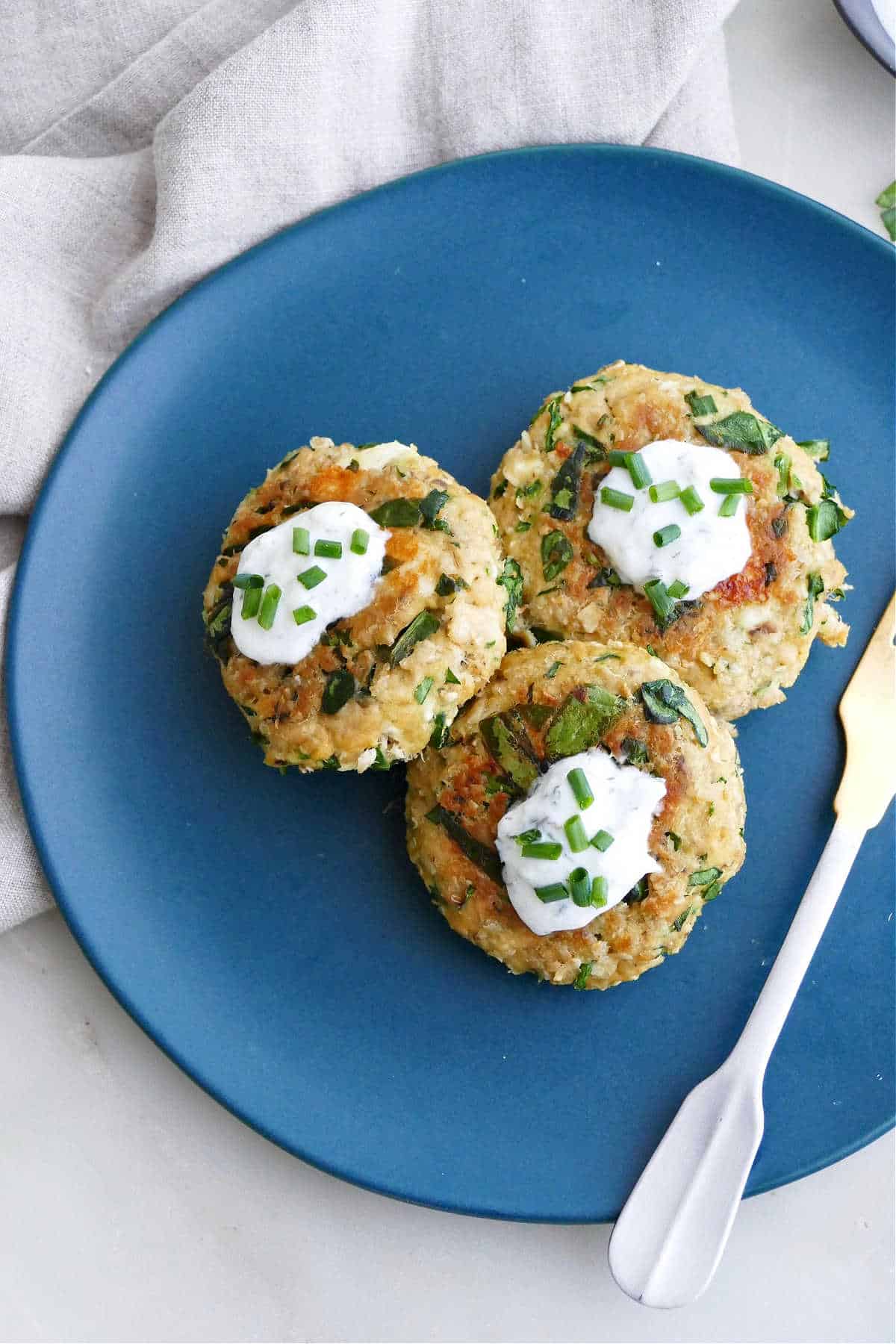 three spinach feta salmon burgers on a serving plate topped with yogurt and chives