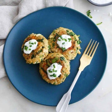 three spinach feta salmon burgers on a serving plate topped with yogurt and chives