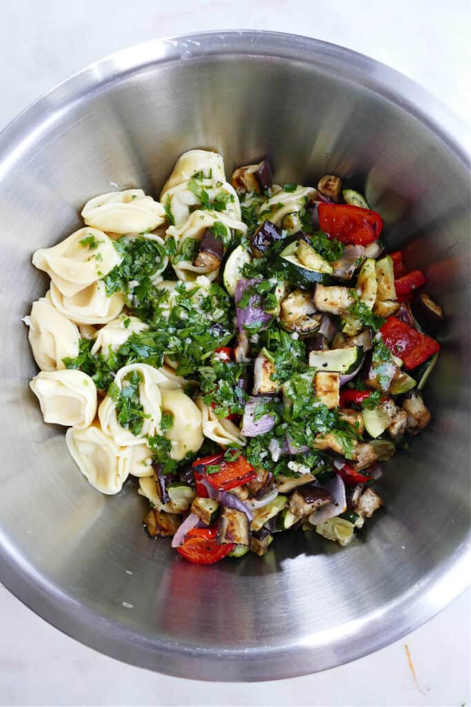 tortellini, roasted vegetables, herbs, and dressing in a mixing bowl
