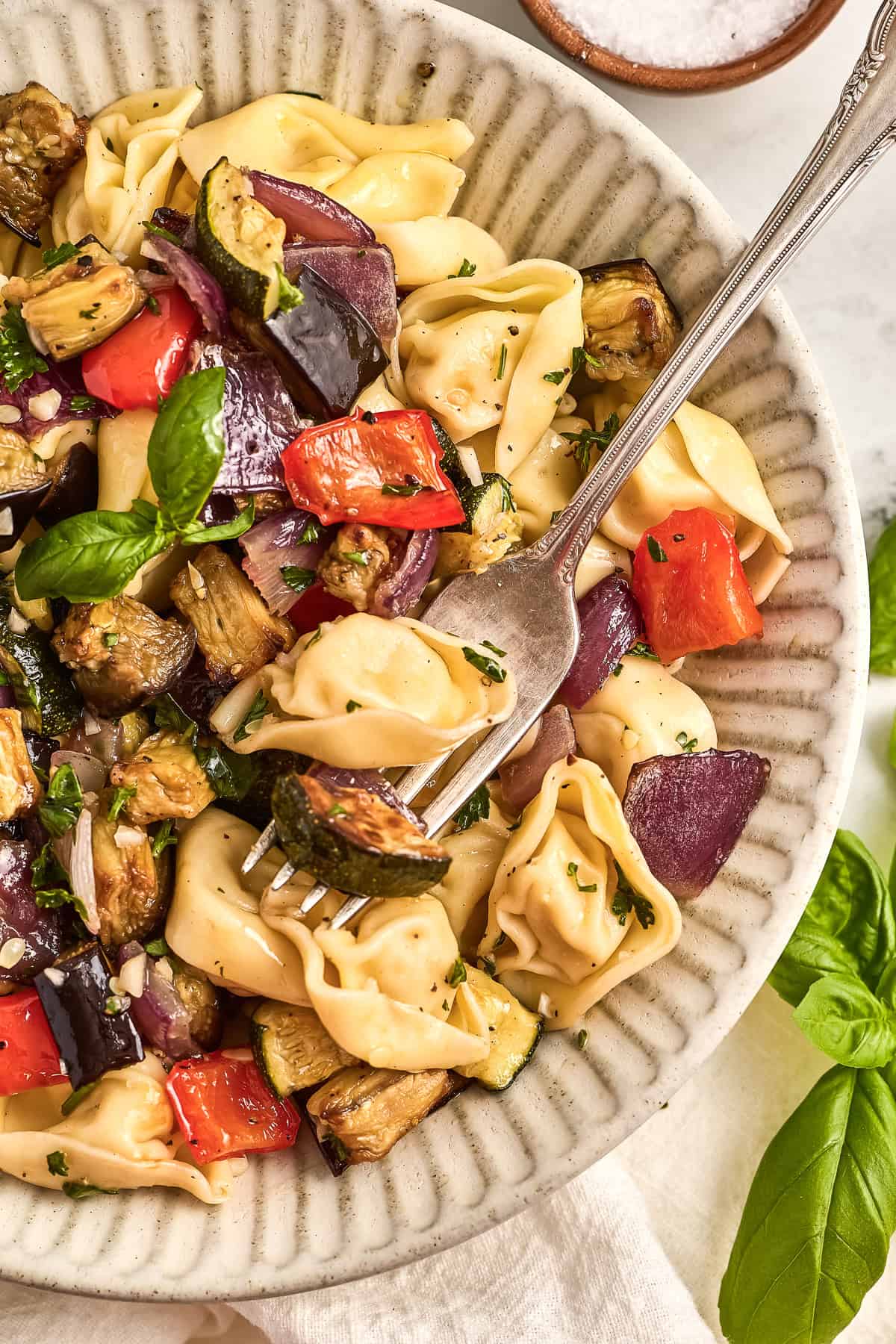 A fork scooping tortellini and roasted vegetable salad with olive oil dressing.