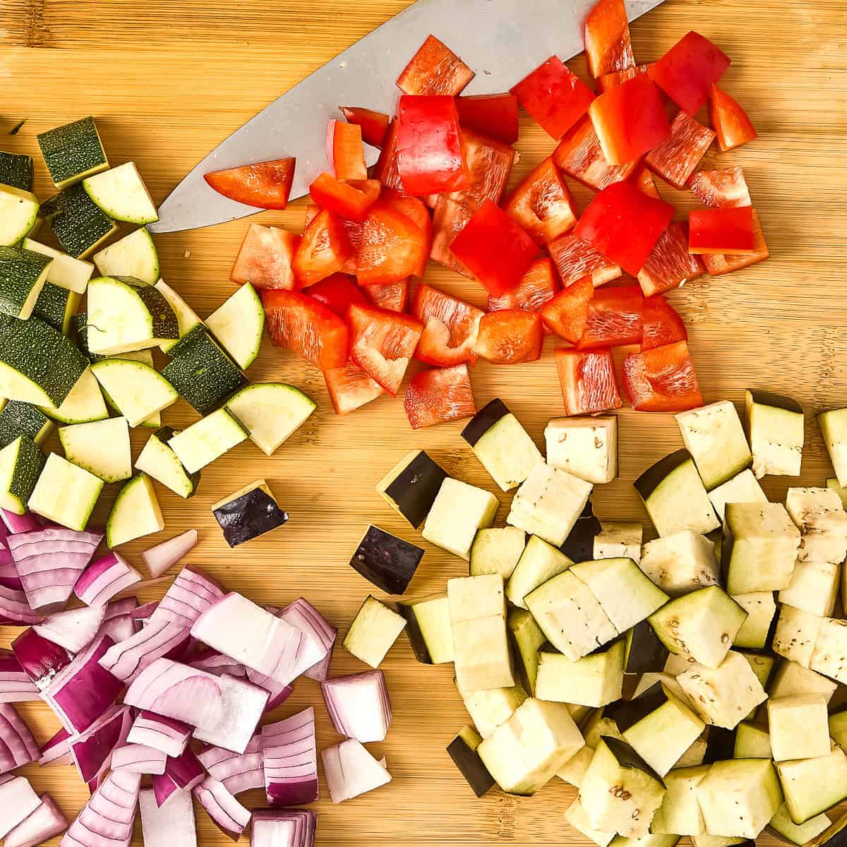 Zucchini, pepper, onion, and eggplant cut into cubes on a cutting board.