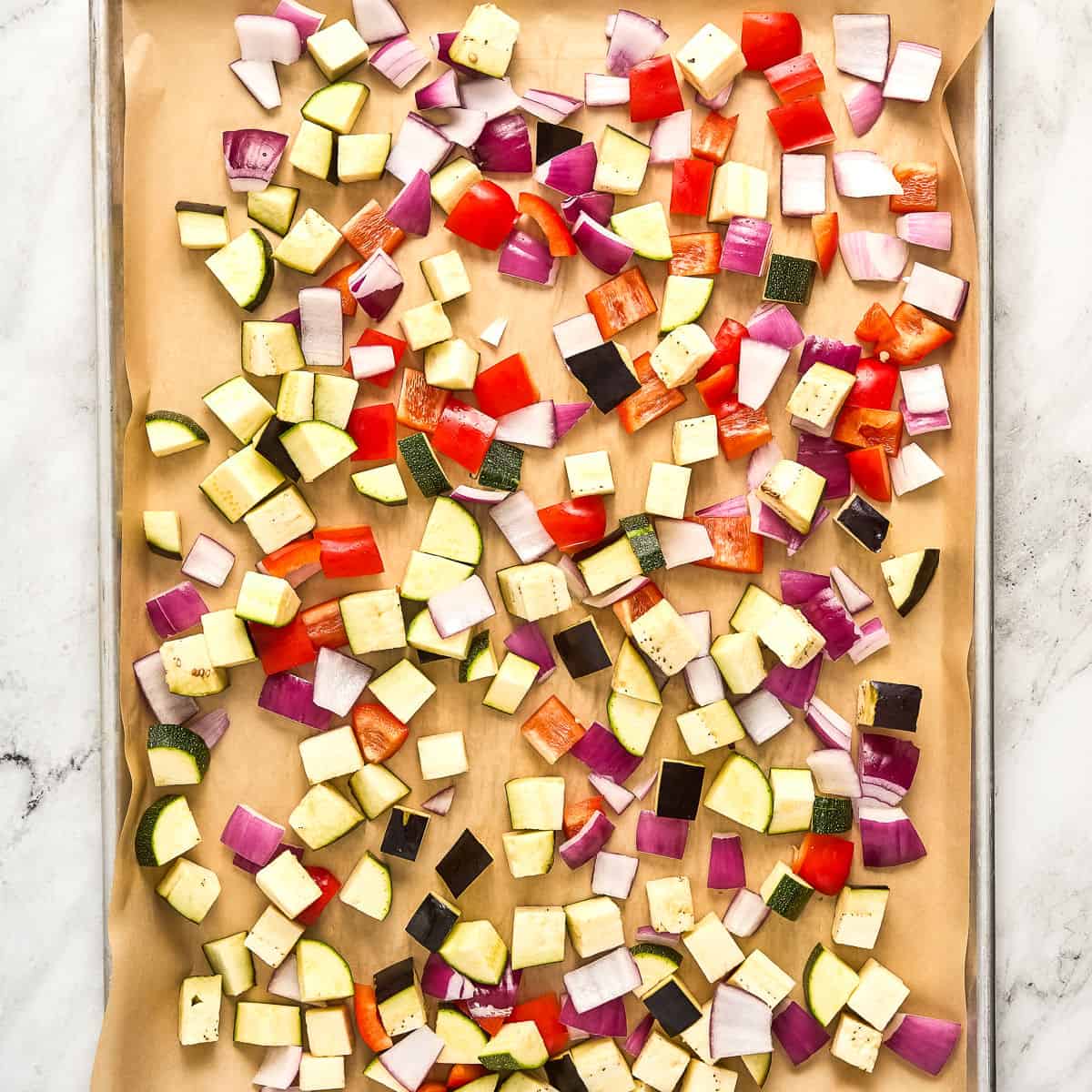 Cubed summer vegetables on a baking sheet lined with parchment paper.