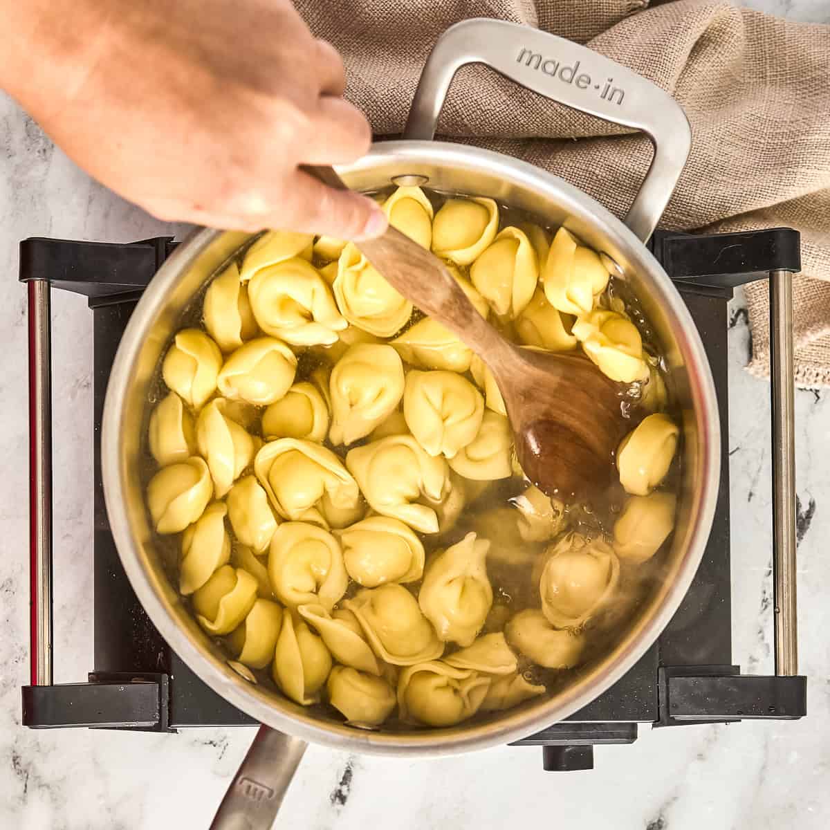 Woman stirring cheese tortellini with a wooden spoon in a pot of boiling water.