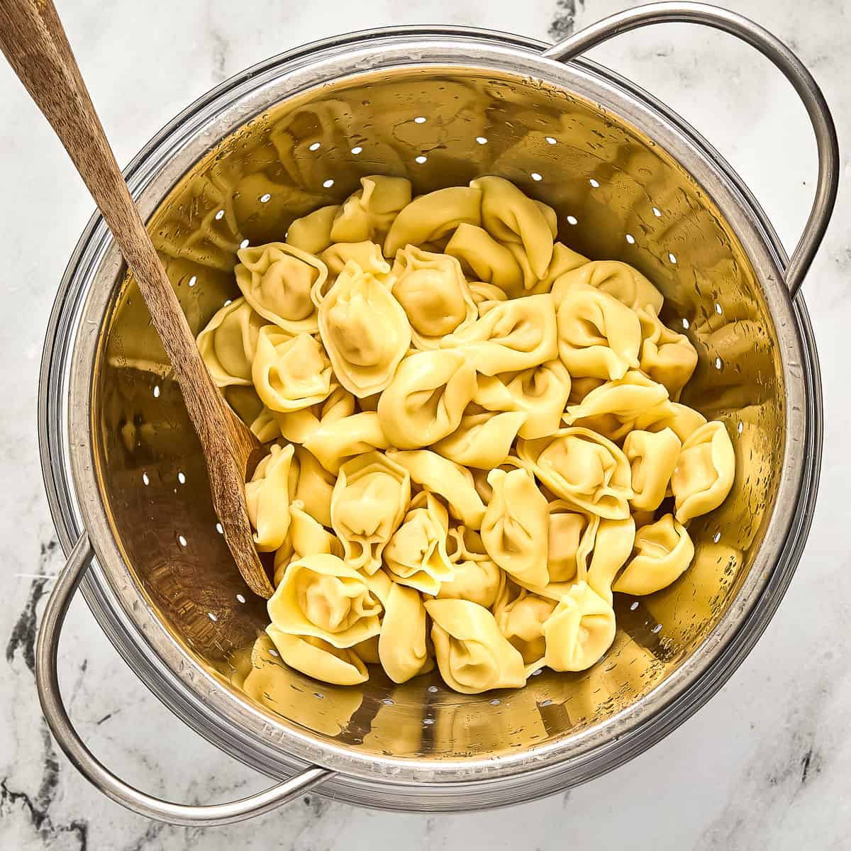 Cheese tortellini in a colander with a spoon after being cooked and drained.