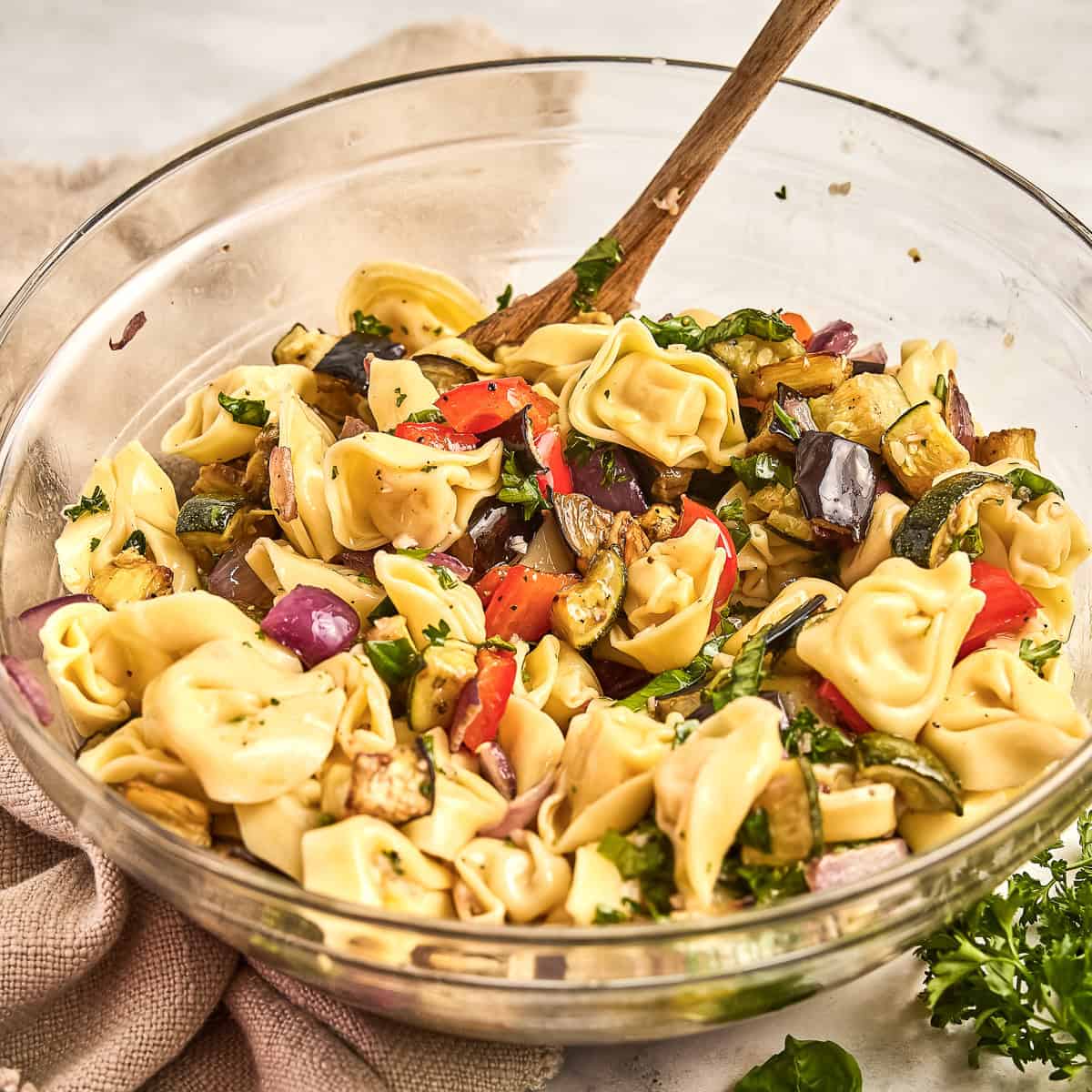 Summer tortellini salad recipe in a mixing bowl with a wooden spoon.