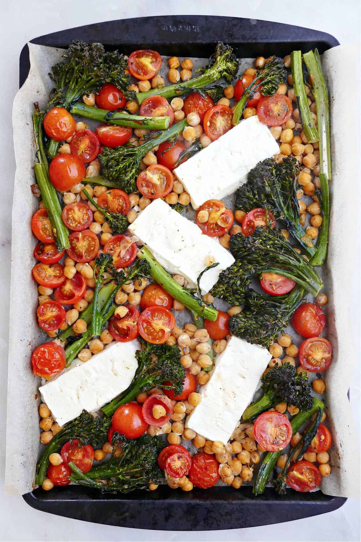 feta, vegetables, and chickpeas spread out on a baking sheet lined with parchment paper