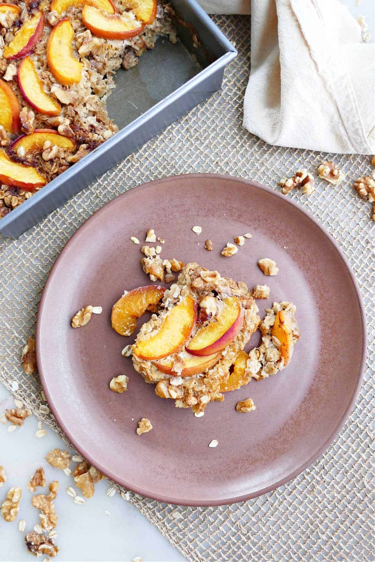 serving of baked peach oatmeal on a dish next to a baking dish with the rest of it