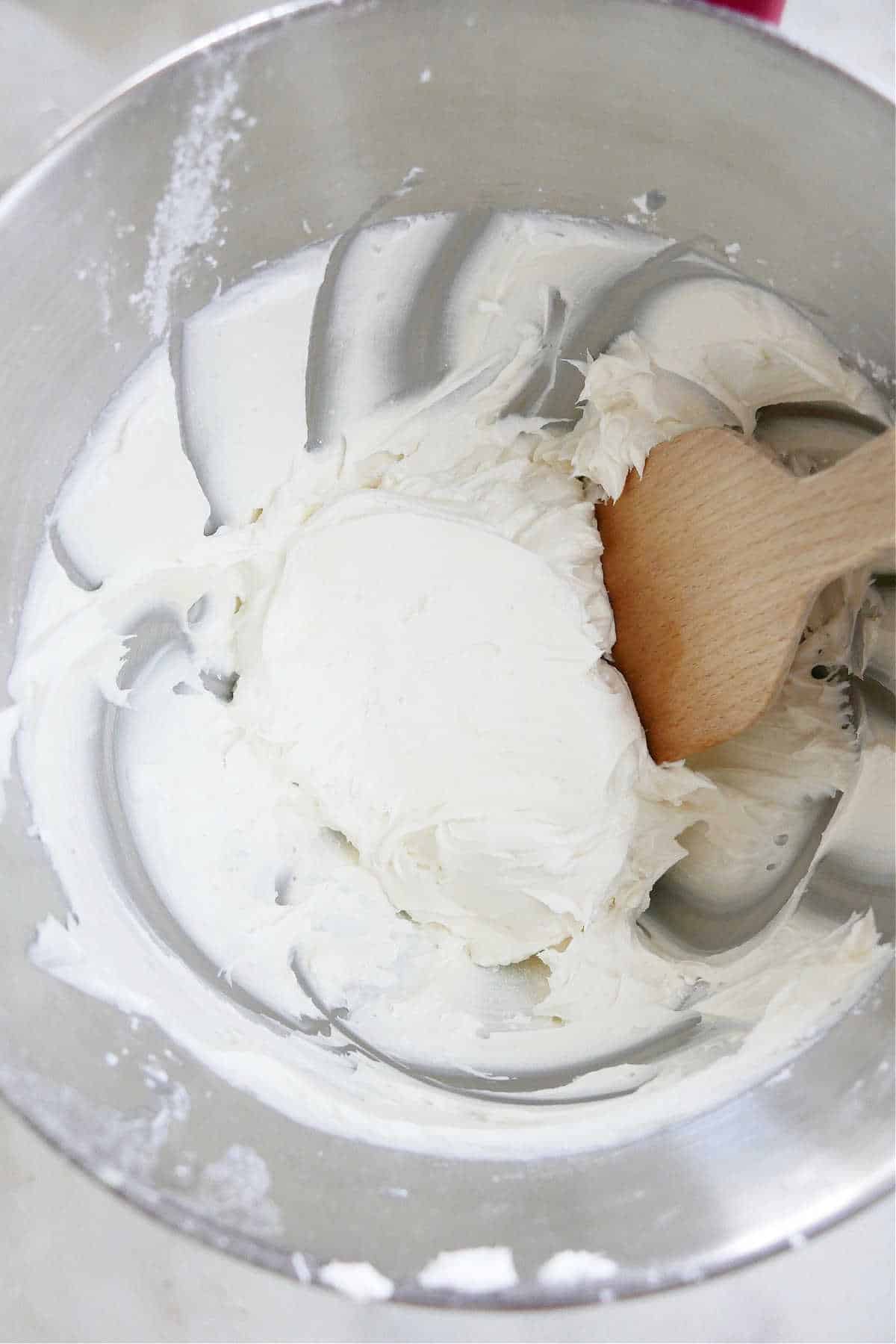 coconut buttercream frosting being mixed with a wooden spatula in a kitchenaid bowl