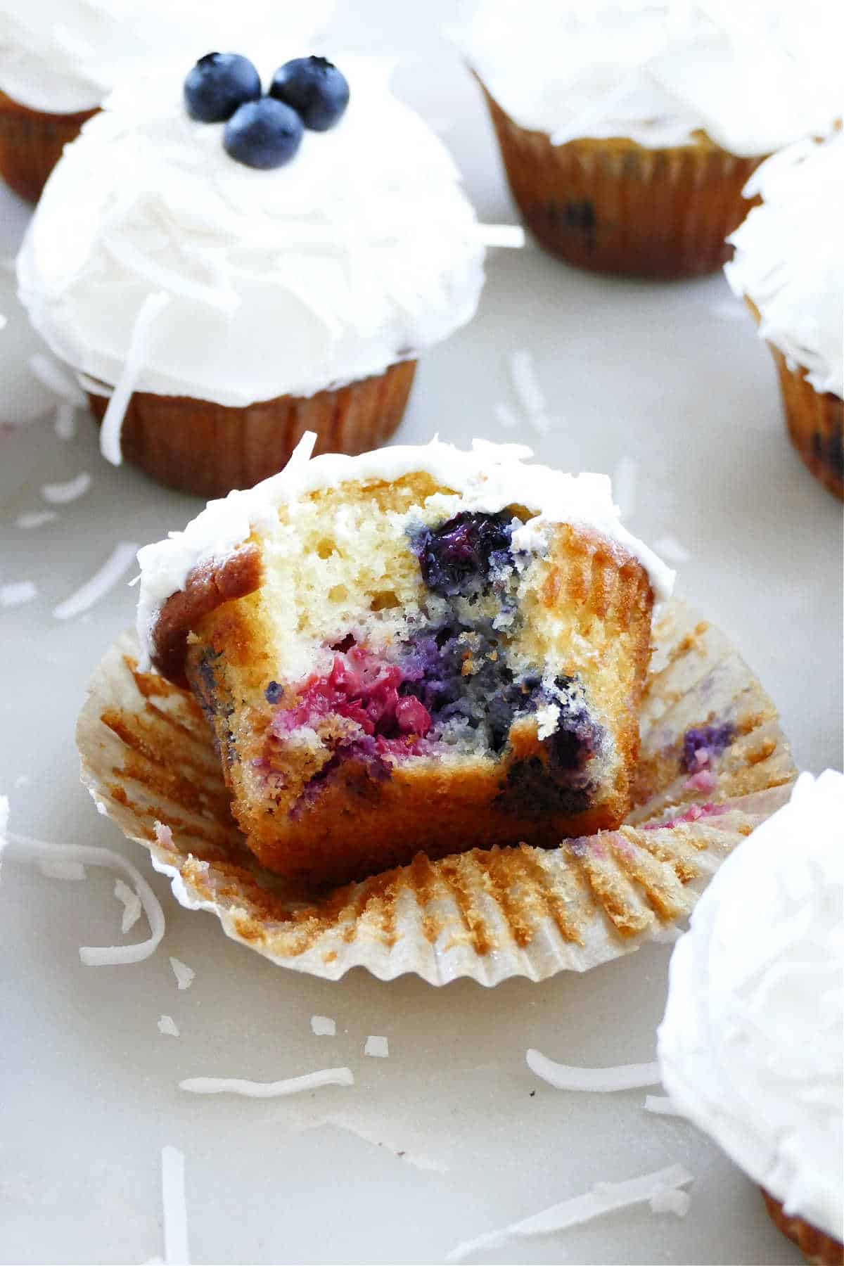 a triple berry cupcake with a bite taken out on a cupcake liner on a counter