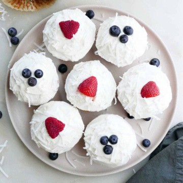 seven berry cupcakes on a circular serving platter next to a sliced cupcake and napkin