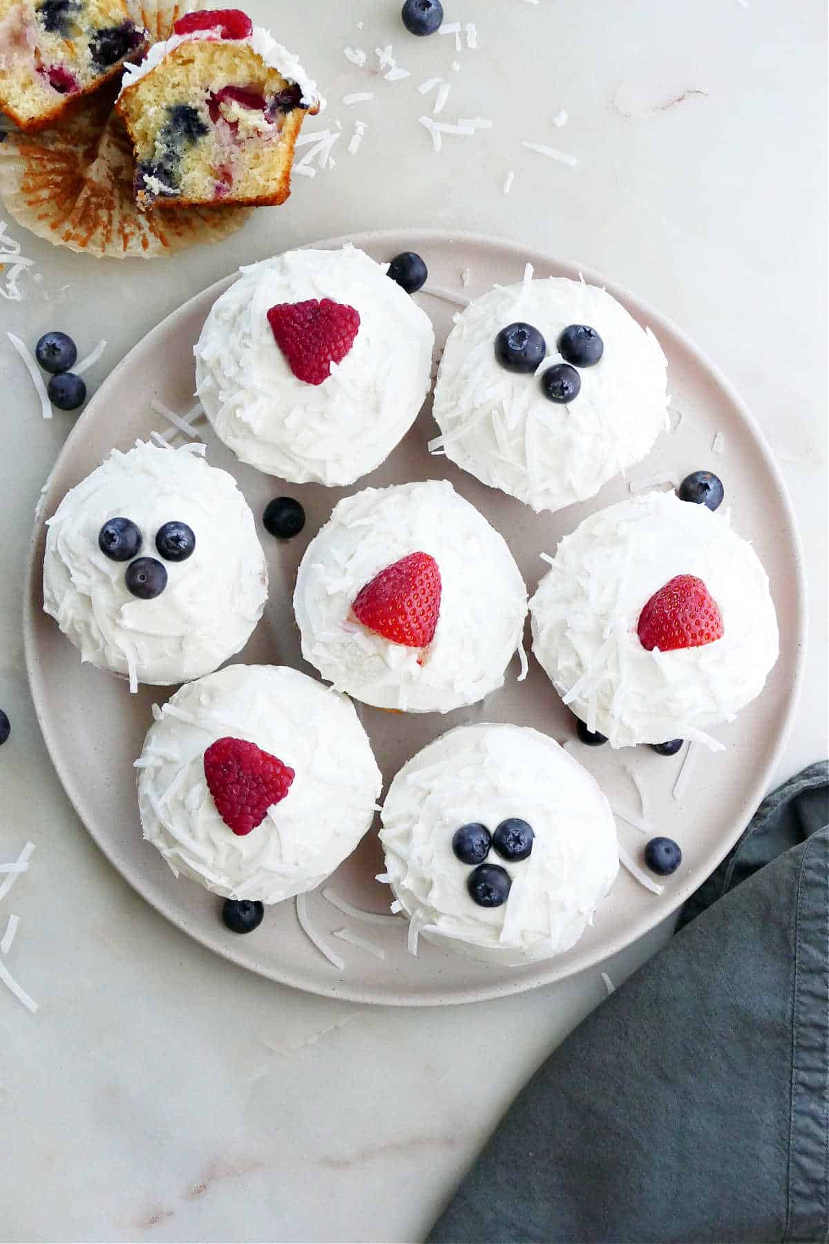 seven berry cupcakes on a circular serving platter next to a sliced cupcake and napkin