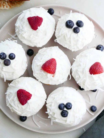 seven berry cupcakes on a circular serving platter next to a sliced cupcake and napkin