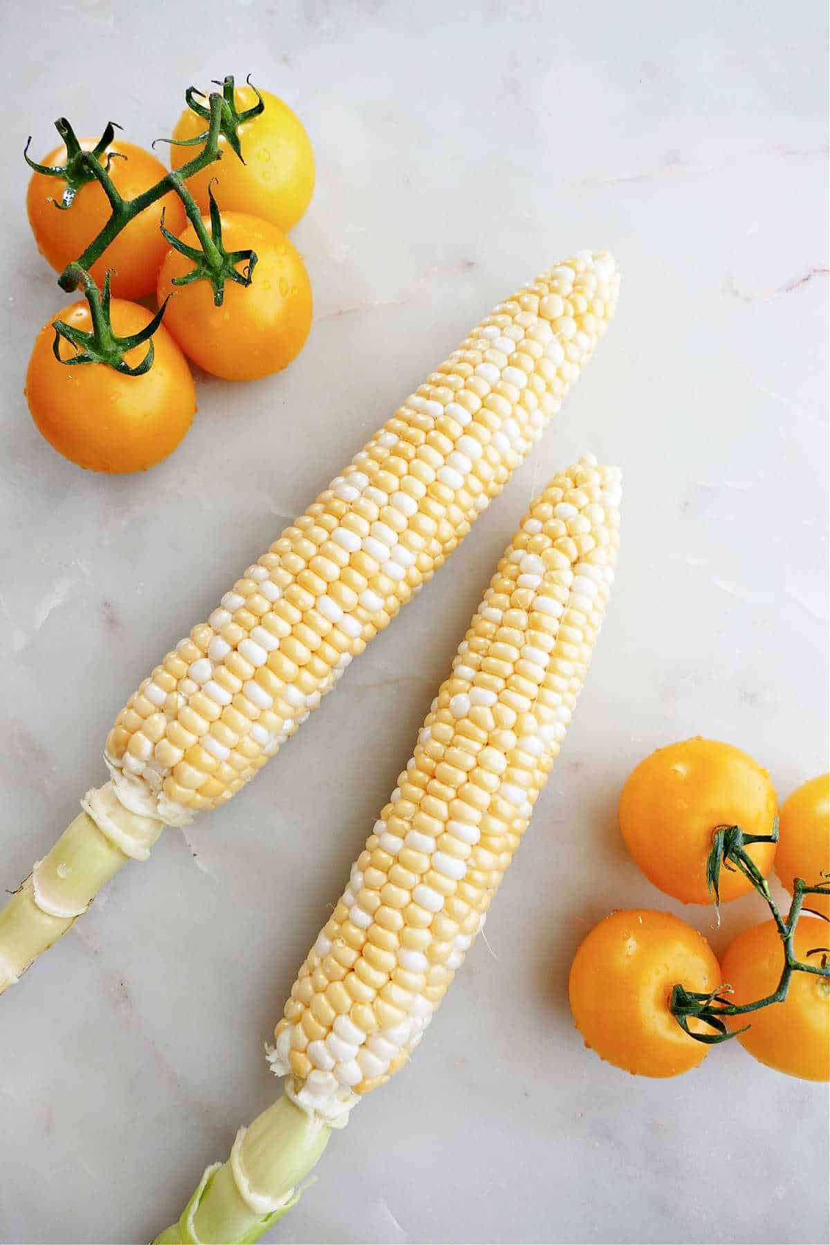 corn on the cob and yellow tomatoes spread out next to each other on a counter