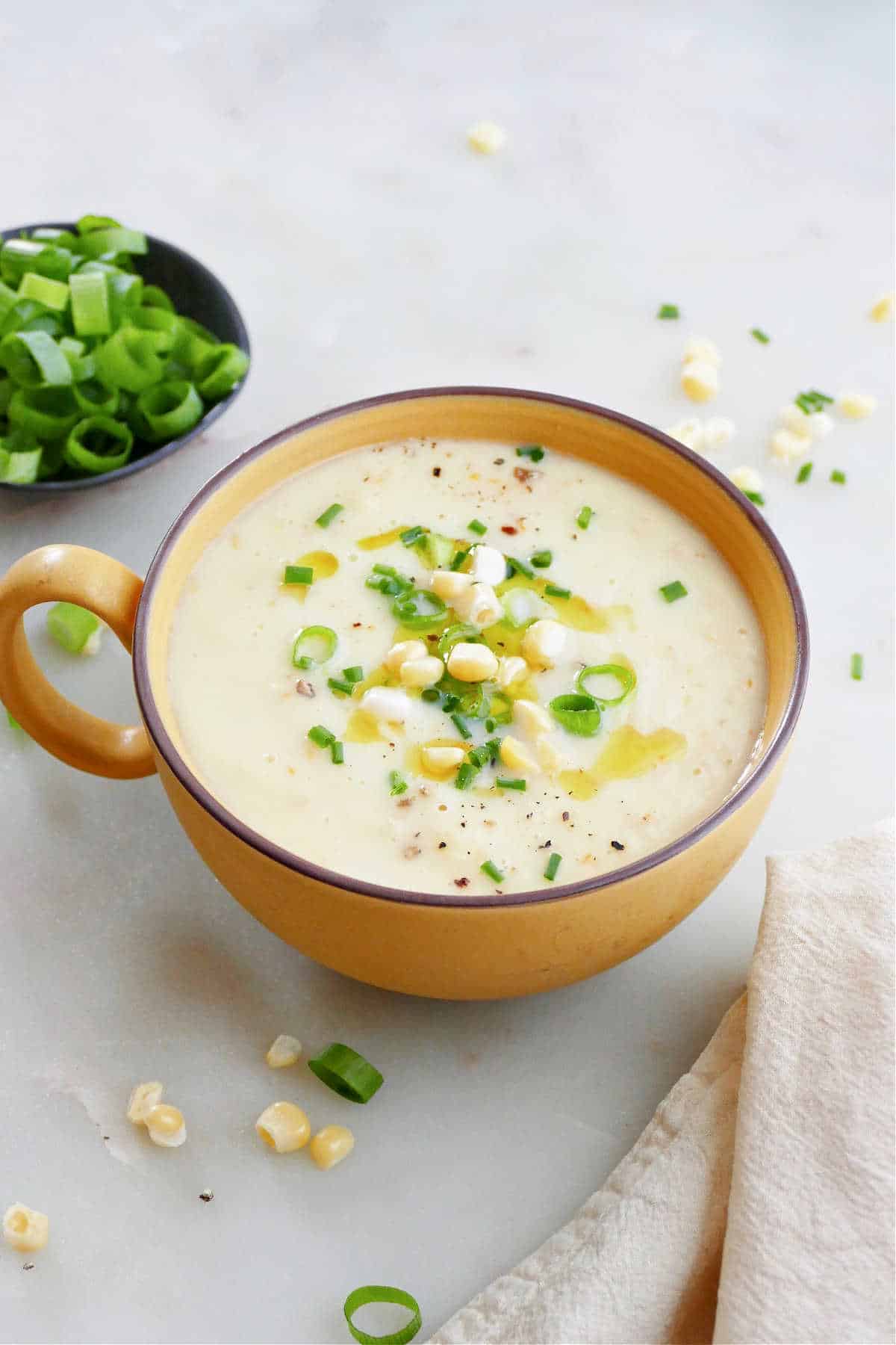 tomato and corn gazpacho in a serving bowl with toppings on a counter