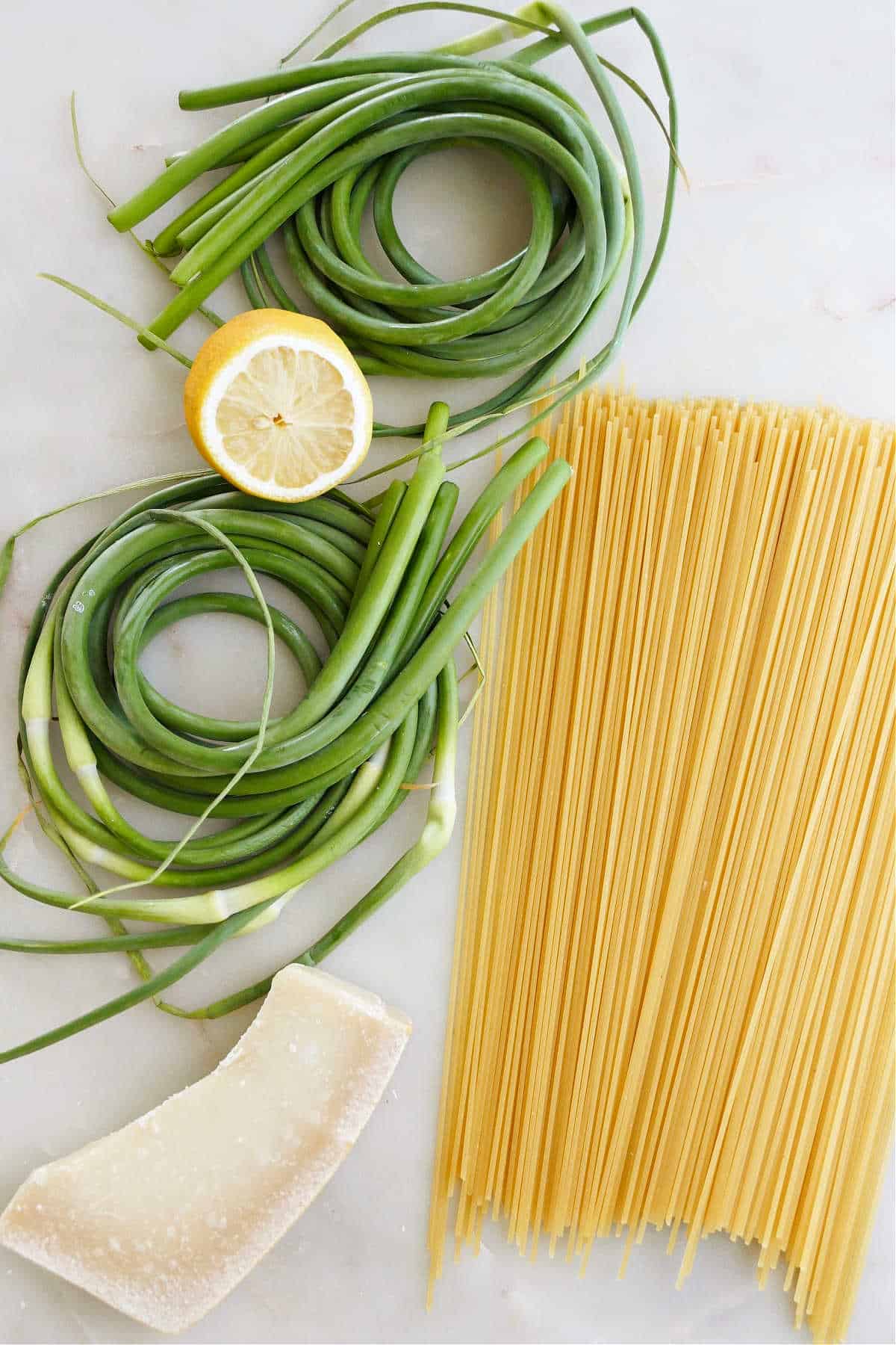 garlic scapes, lemon, spaghetti, and parmesan spread out next to each other on a counter