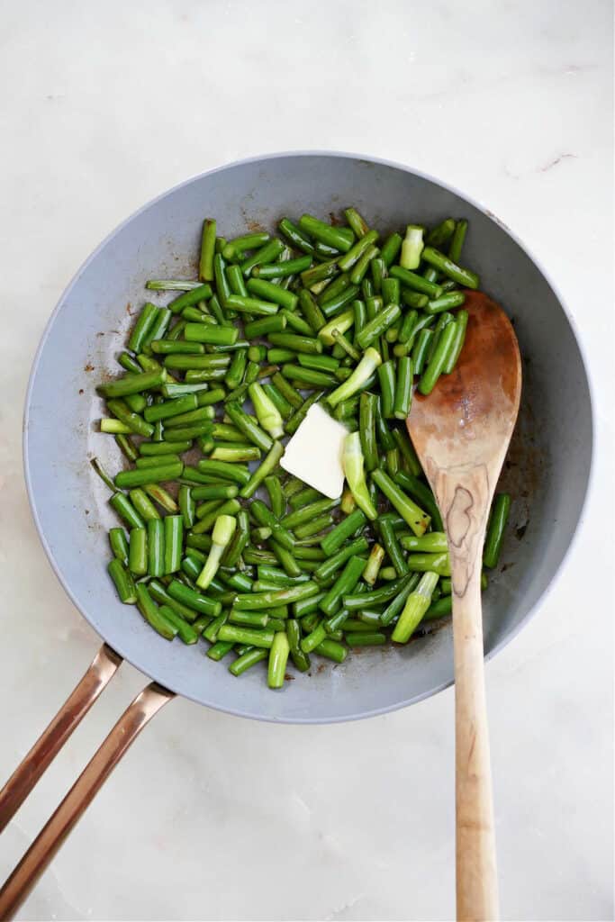 chopped garlic scapes cooking in a skillet with a pat of butter