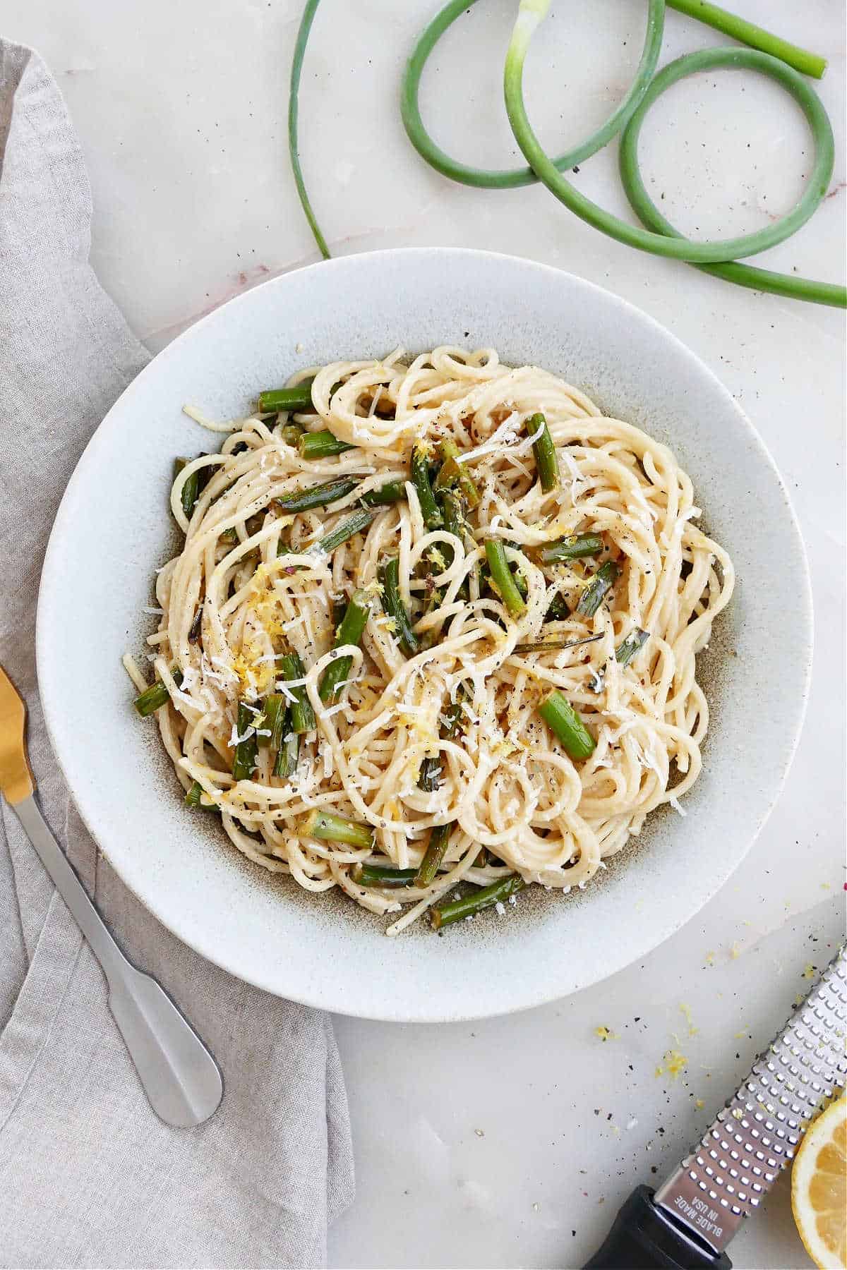 garlic scape pasta topped with lemon zest and cheese in a serving bowl