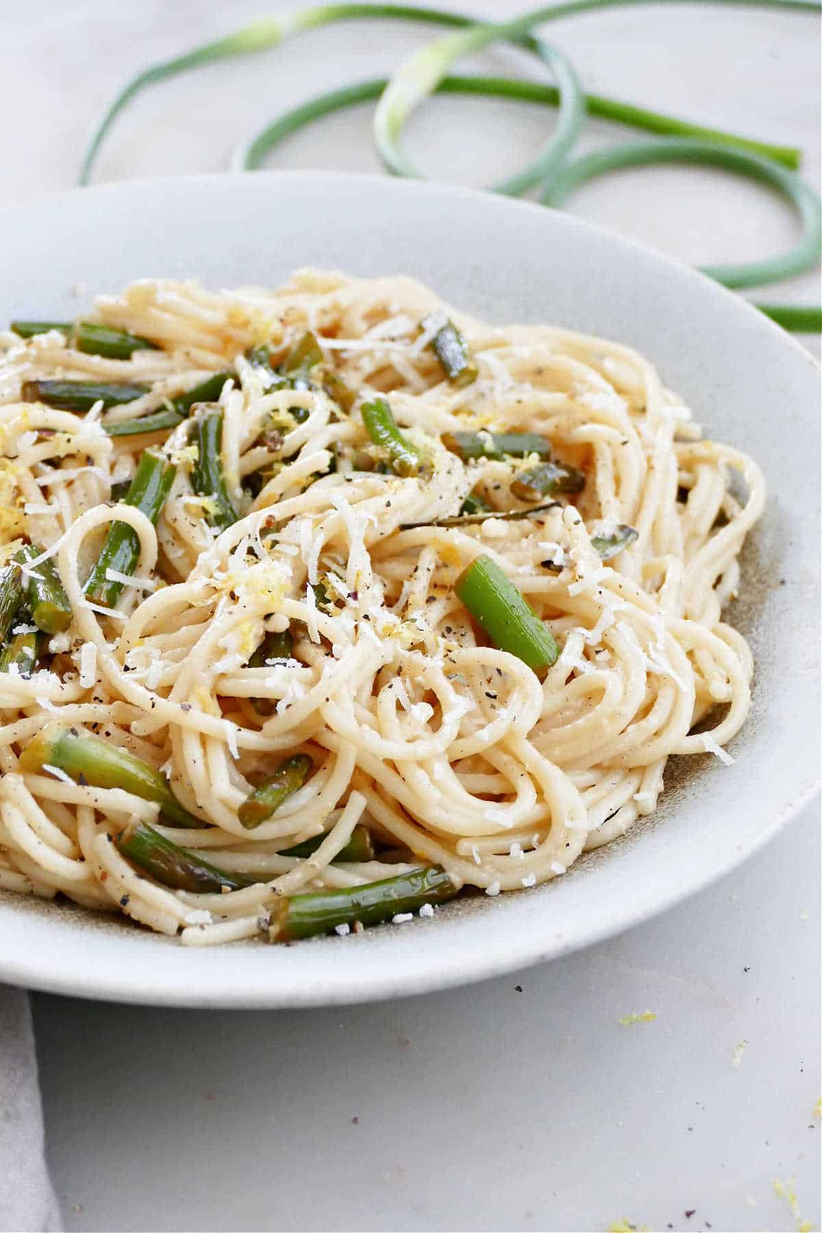 side angle of garlic scape pasta with lemon zest and cheese in a bowl