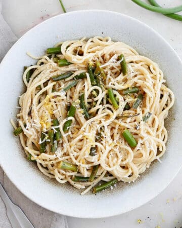 garlic scape pasta topped with lemon zest and cheese in a serving bowl