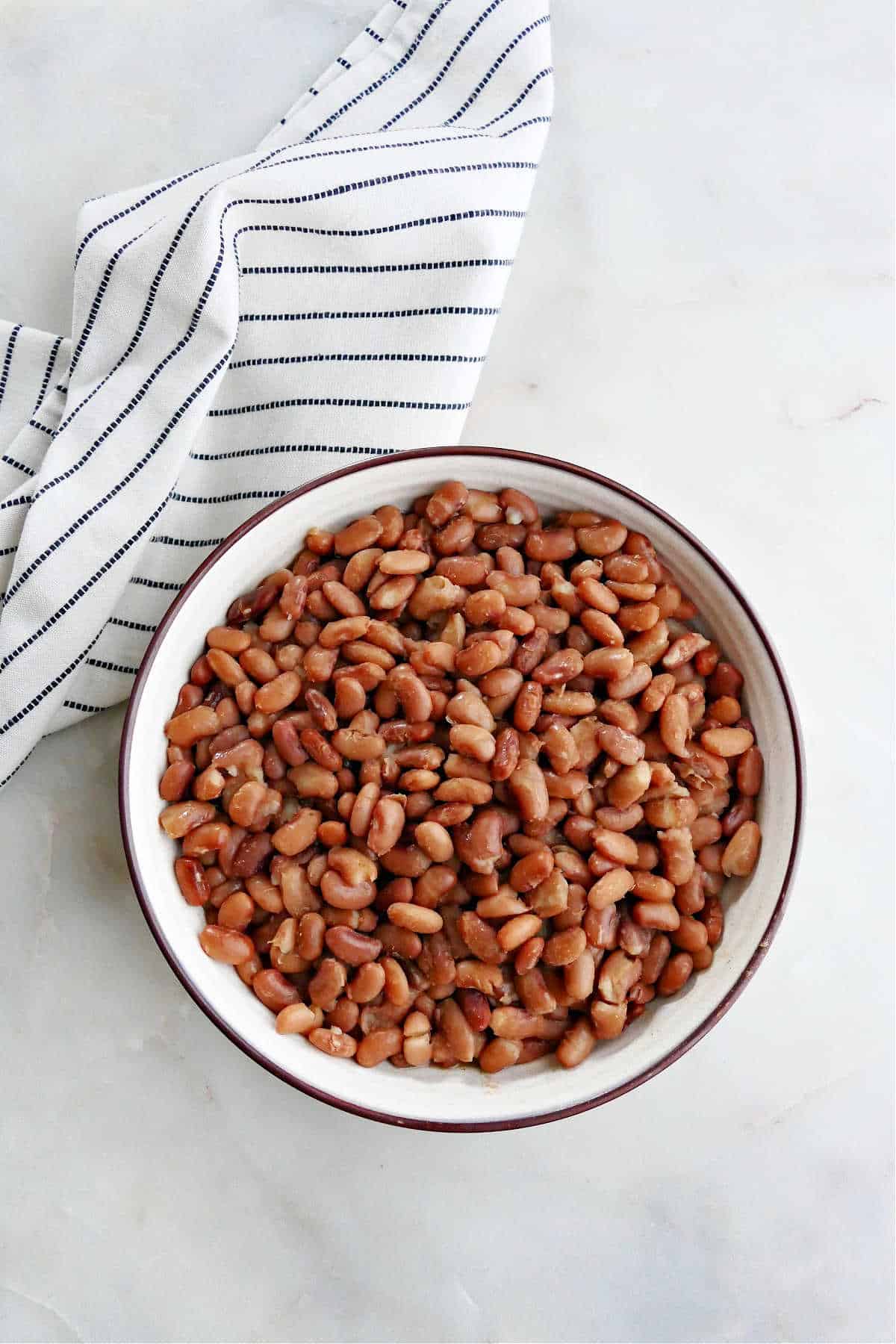 Instant Pot pinto beans in a serving bowl on a counter next to a striped napkin
