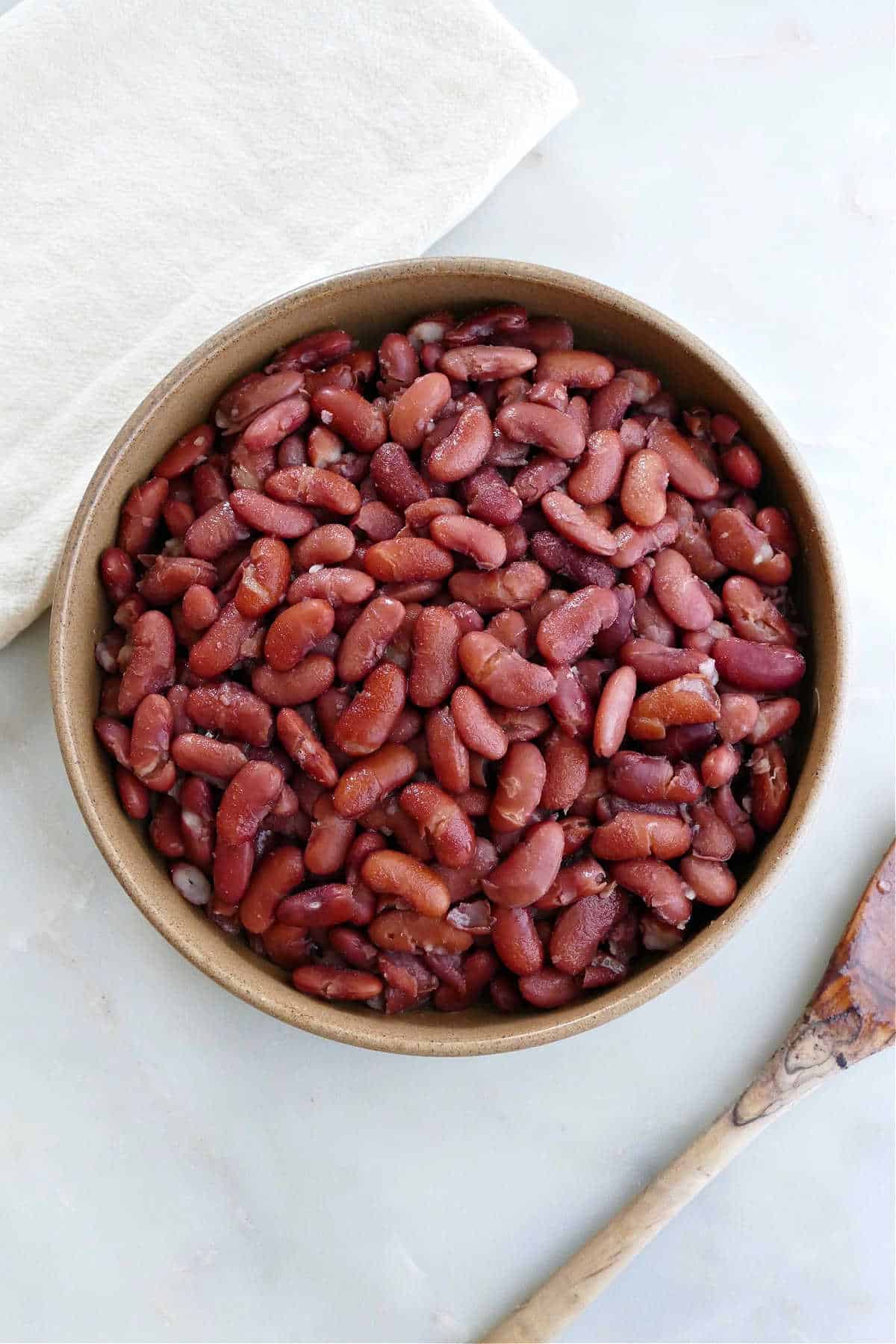 cooked kidney beans in a serving bowl next to a spoon and napkin