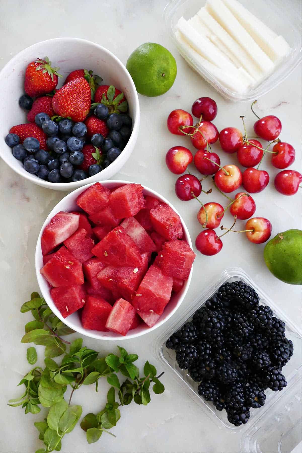 berries, watermelon, lime, jicama, cherries, and mint spread out on a counter