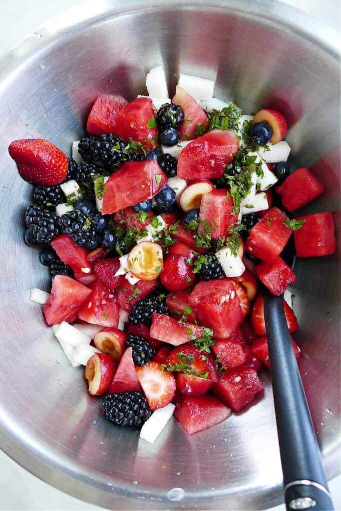 fruit salad mixed together and drizzled with a mint lime dressing in a bowl