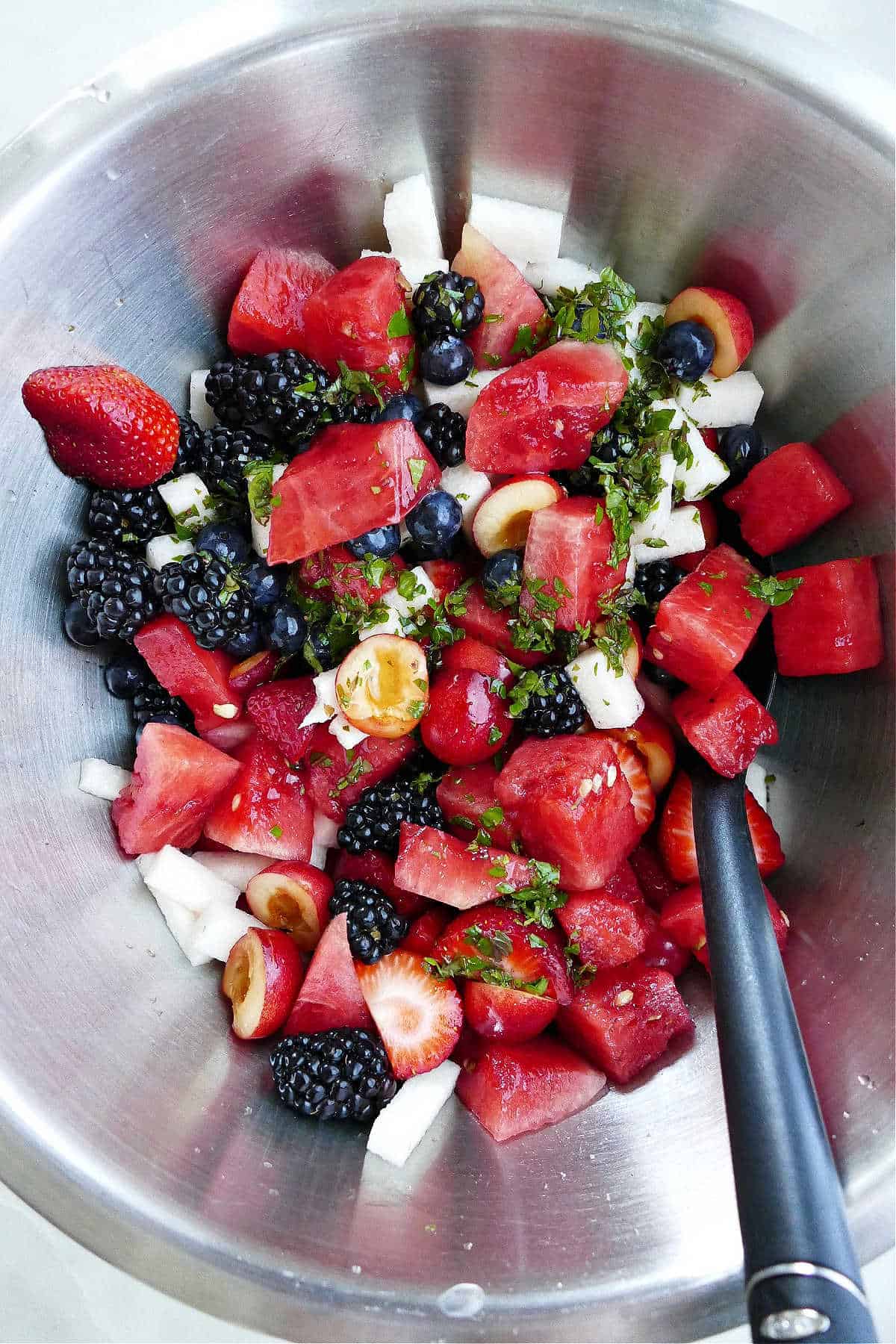 Fruit salad mixed together and drizzled with a mint lime dressing in a bowl.