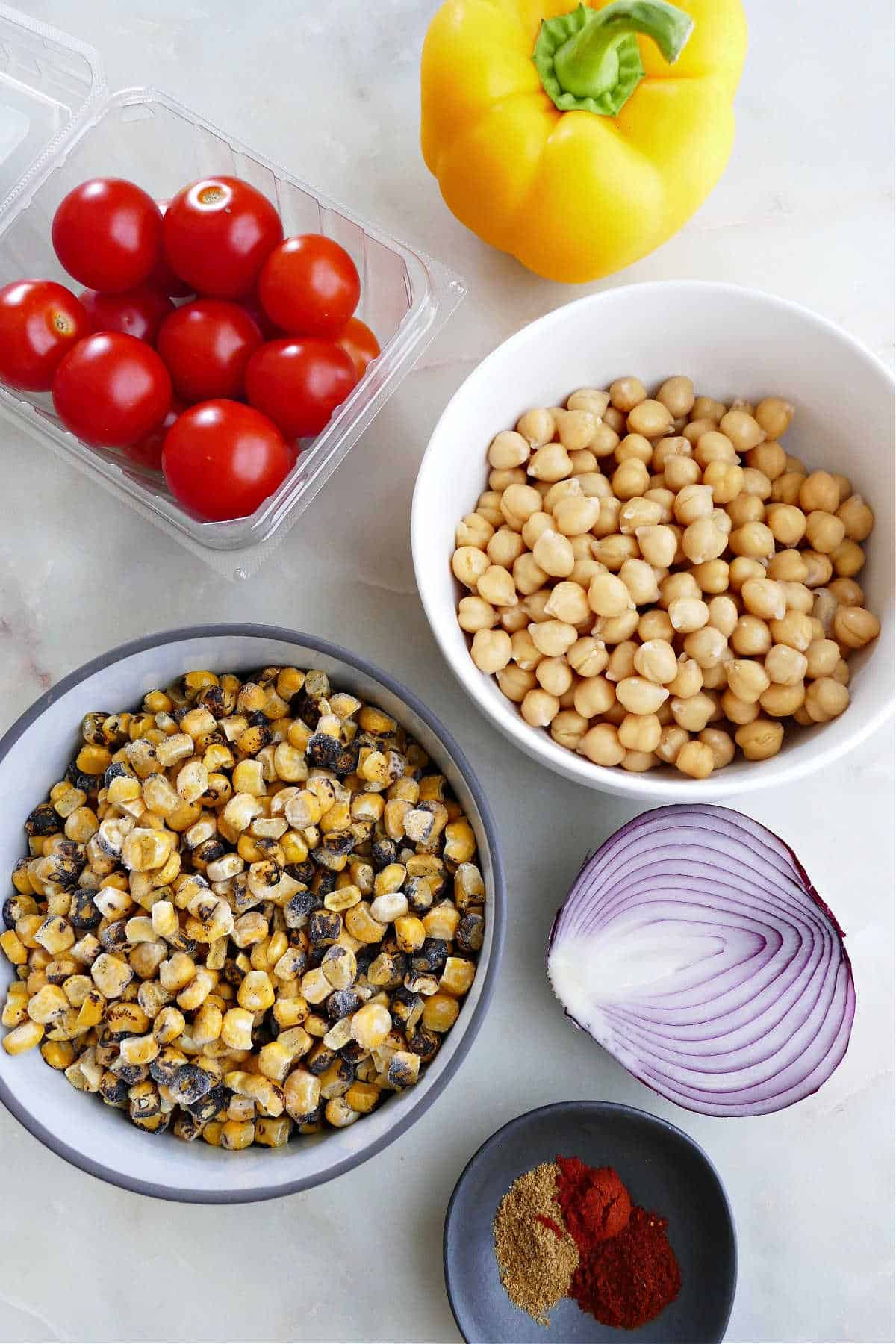 bell pepper, tomatoes, chickpeas, charred corn, red onion, and spices on a counter