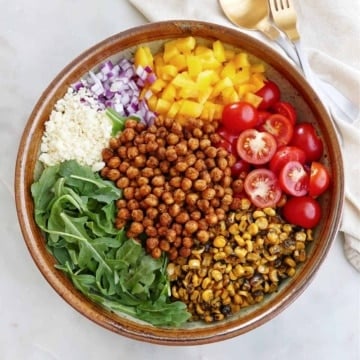 arugula, roasted chickpeas, corn, tomatoes, pepper, onion, and cheese in a large serving bowl