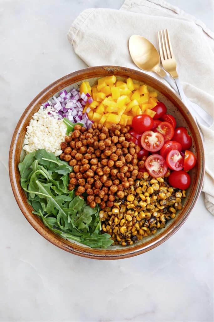 arugula, roasted chickpeas, corn, tomatoes, pepper, onion, and cheese in a large serving bowl